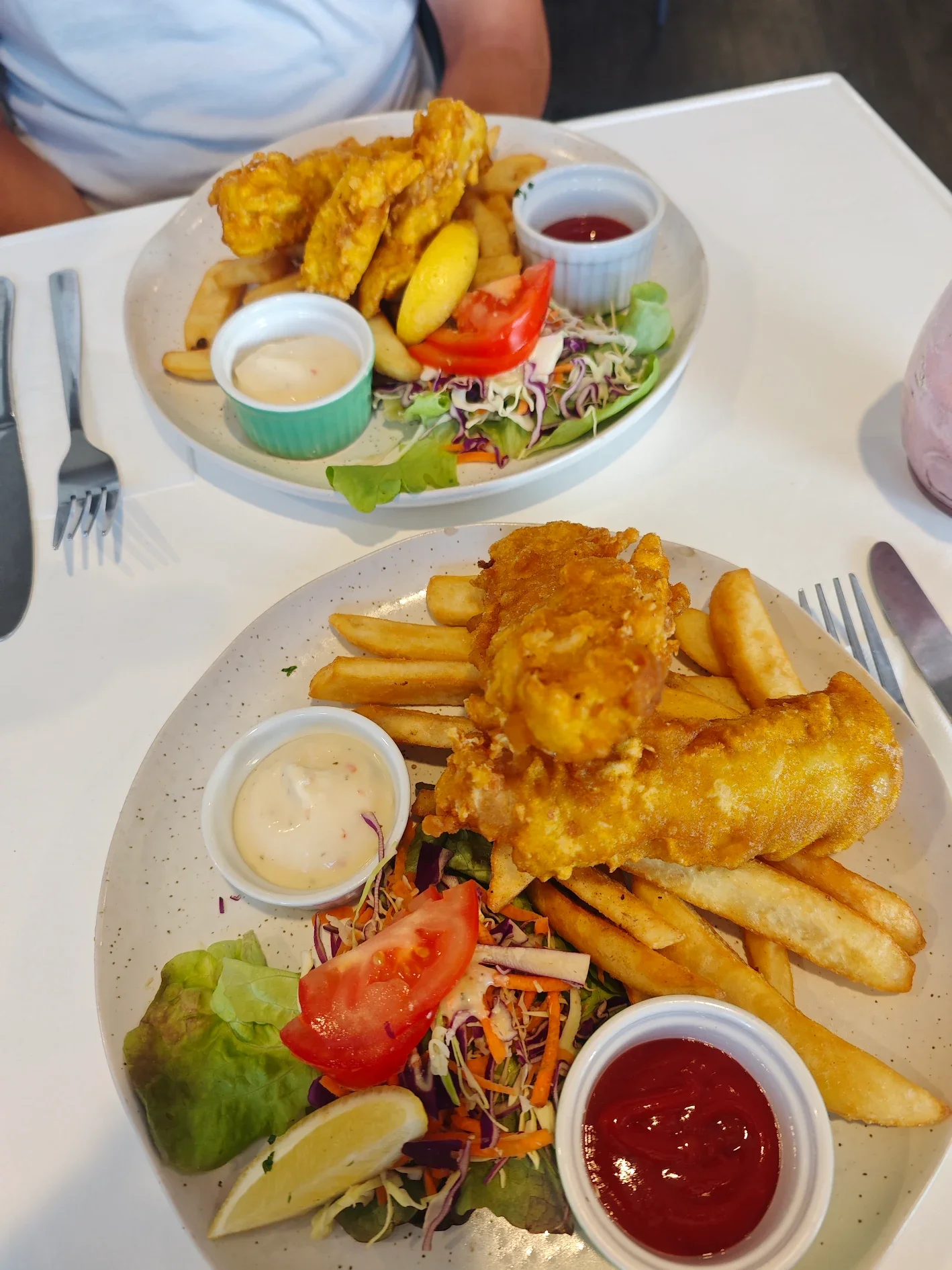 Two plates of fish and chips with coleslaw, ketchup, and tartar sauce at a restaurant table from stone oven bakery in hokitika