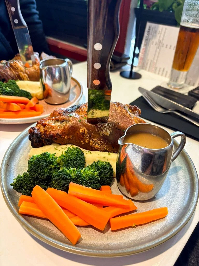 Steak with broccoli, carrots, mashed potatoes, gravy, and a small pitcher of sauce on a metal plate, with a knife stuck into the steak.