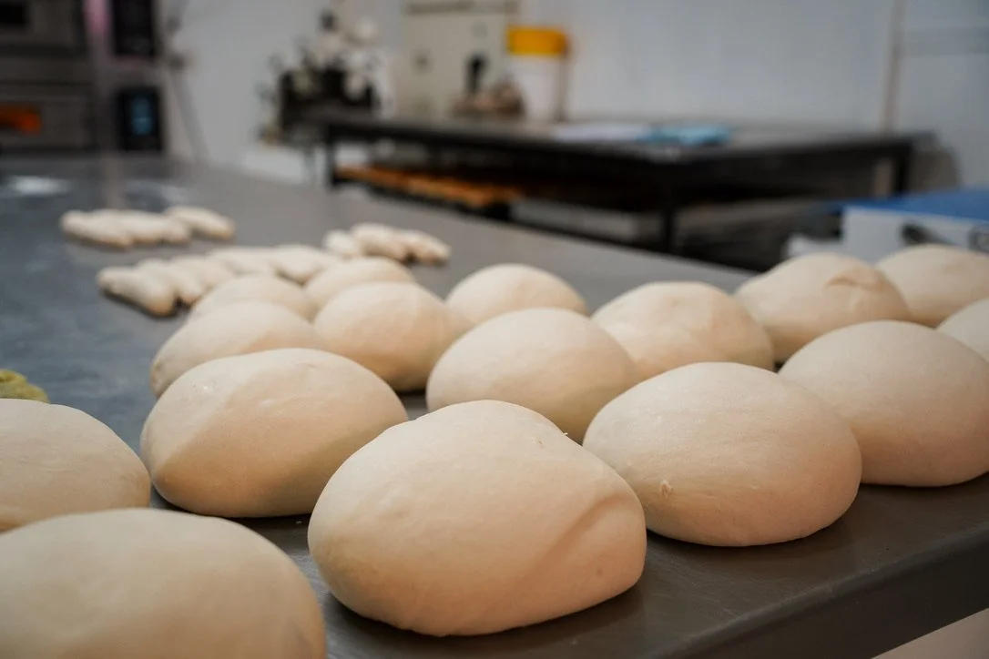 Raw dough balls arranged on a stainless steel countertop in stone oven bakery kitchen.