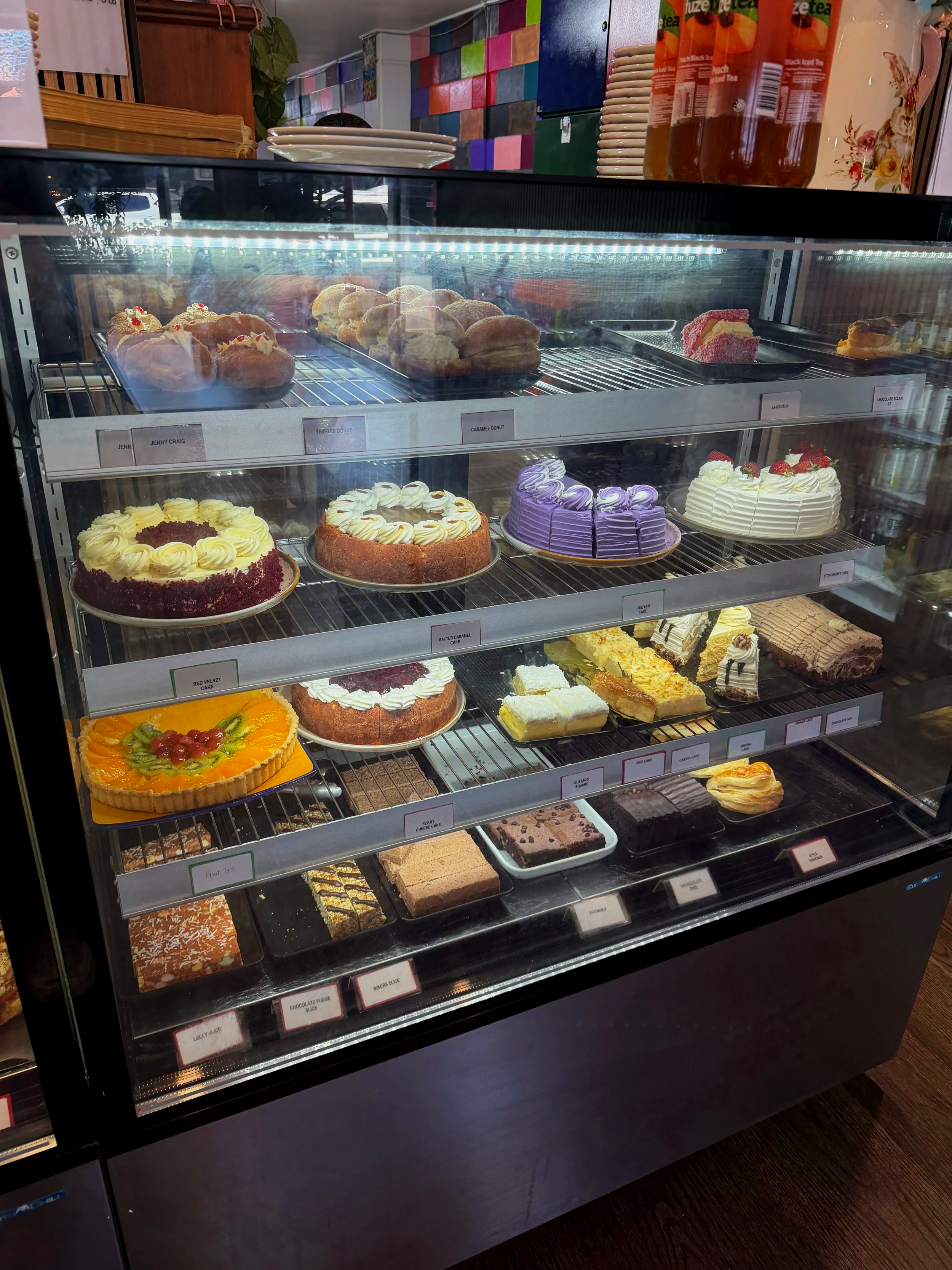 A display case full of various cakes and desserts, including fruit tart, layered cakes, and brownies, inside stone oven bakery and cafe in Hokitika 
