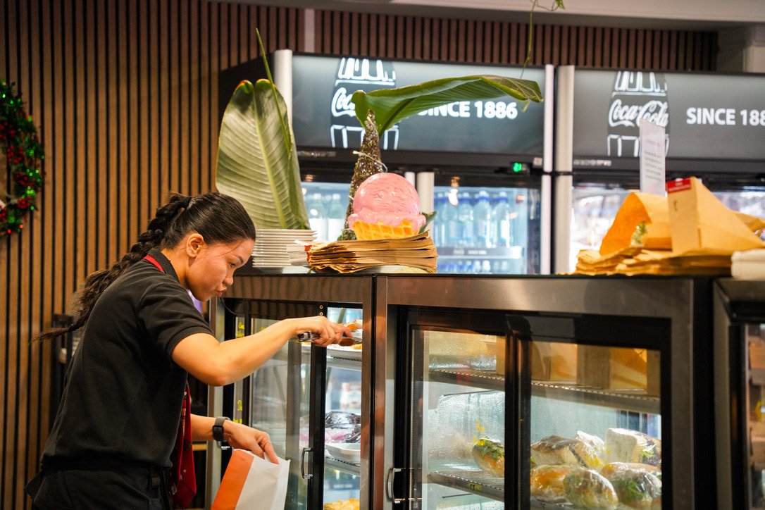 stone oven bakery and cafe staff member, selecting items from a refrigerated display case filled with various bakery cabinet foods.