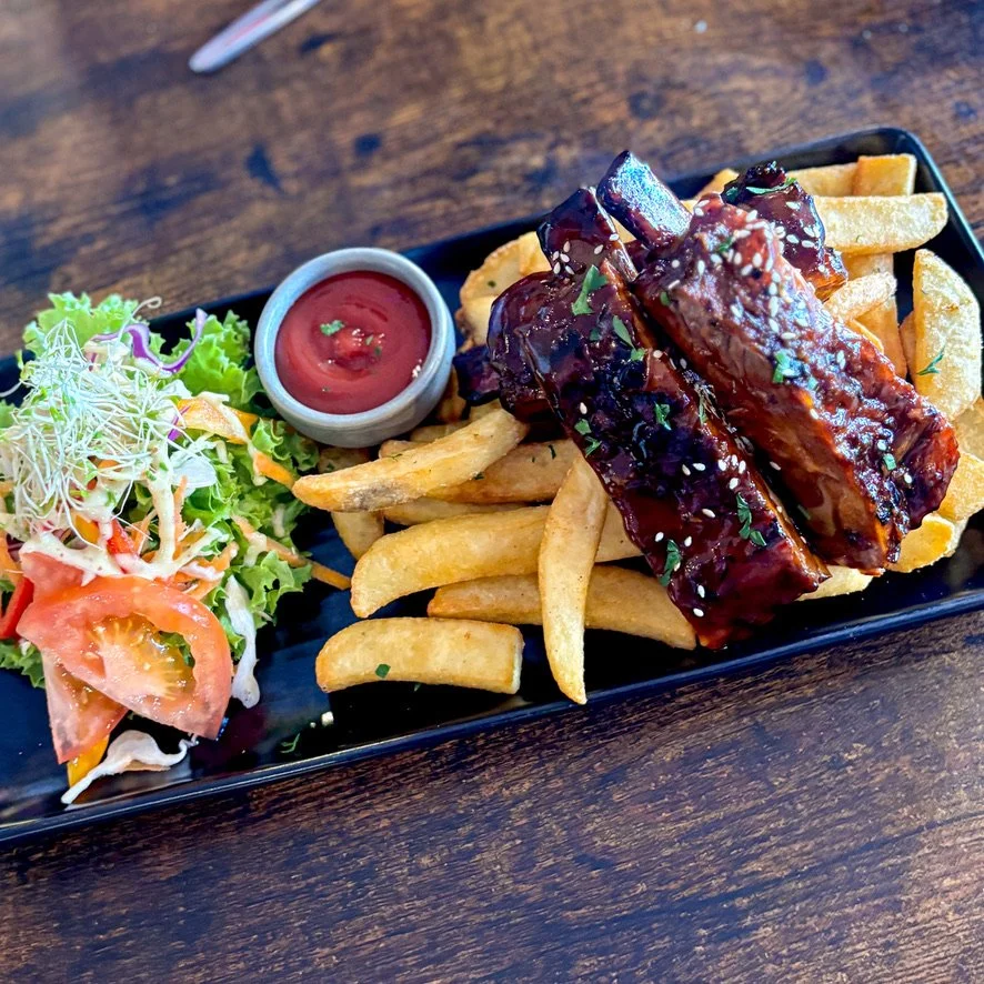 Barbecued ribs with French fries, a side salad, and ketchup on a black rectangular plate. from stone oven bakery and cafe restaurant in Hokitika
