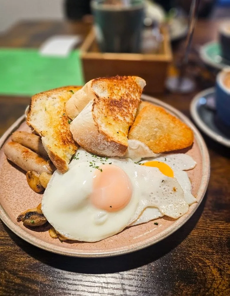 A plate of breakfast food including sunny-side up eggs, toasted bread, and cooked sausage and mushrooms.