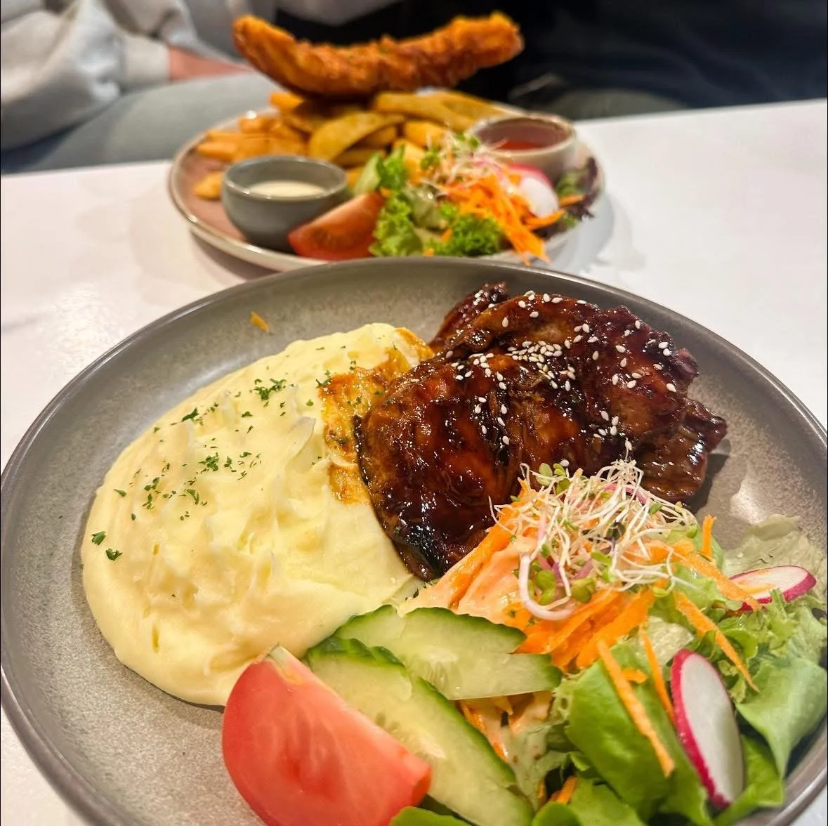 Plate of mashed potatoes with parsley, glazed ribs with sesame seeds, and a fresh salad with cucumbers, radishes, shredded carrots, and sprouts.
