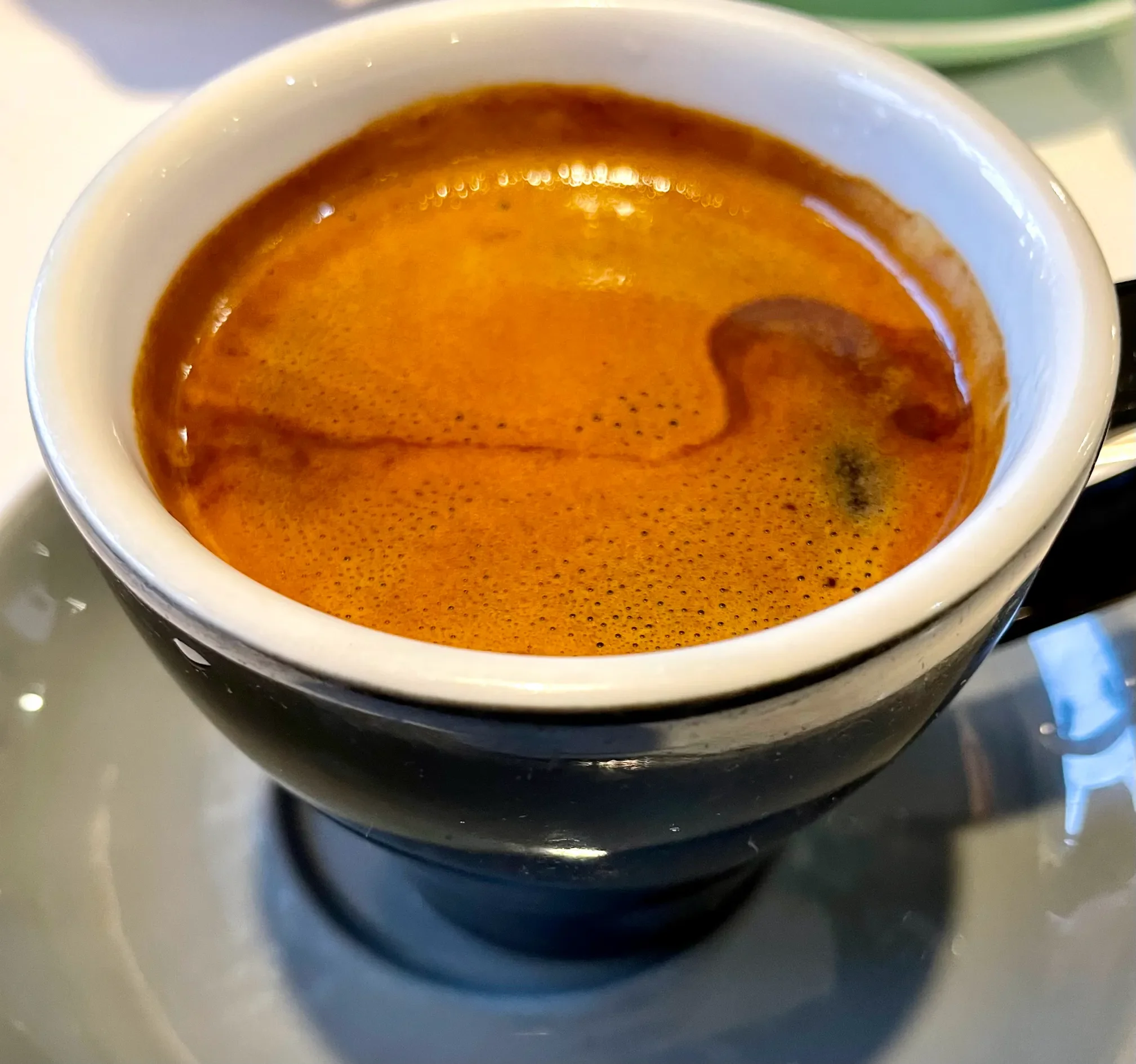 Close-up of a cup of freshly brewed espresso with a layer of crema on top, served on a saucer from stone oven bakery and cafe in hokitika