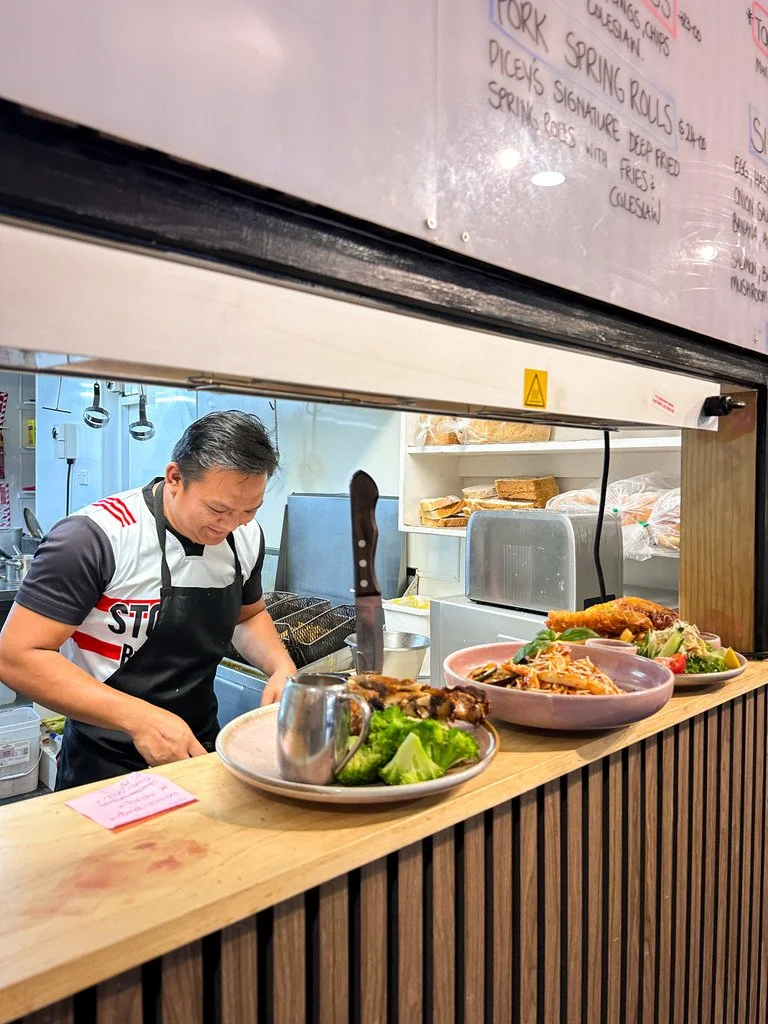 A man cooking in a kitchen behind a wooden counter with plates of salad and food.