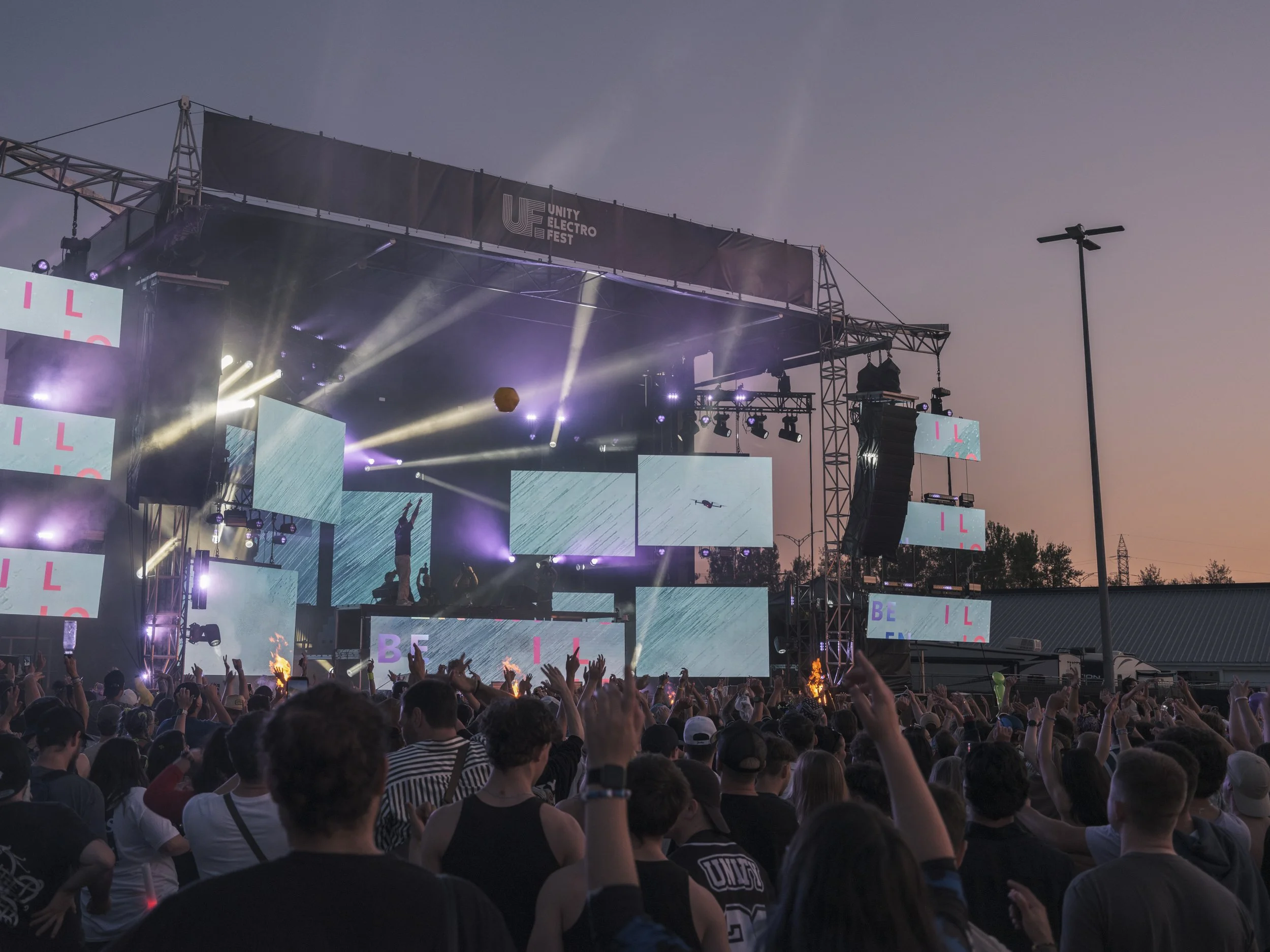 Wide festival crowd scene with large stage screens and evening light at Unity Electrofëst