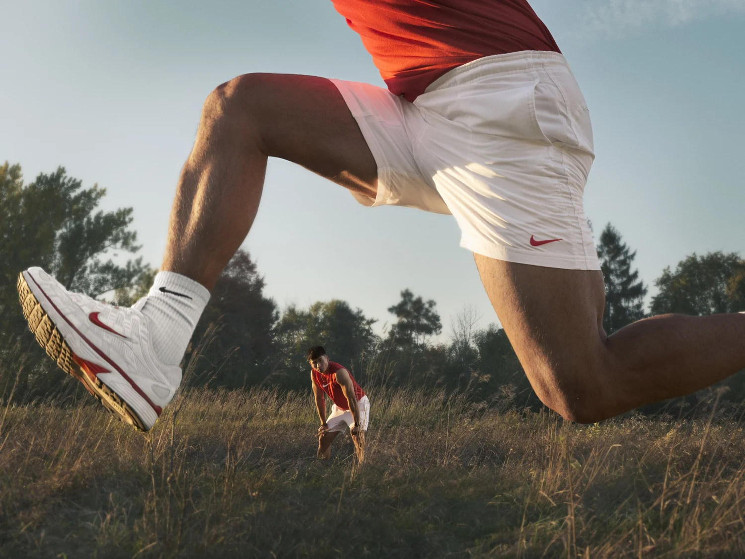 Runner framed through another athlete's stride at dusk