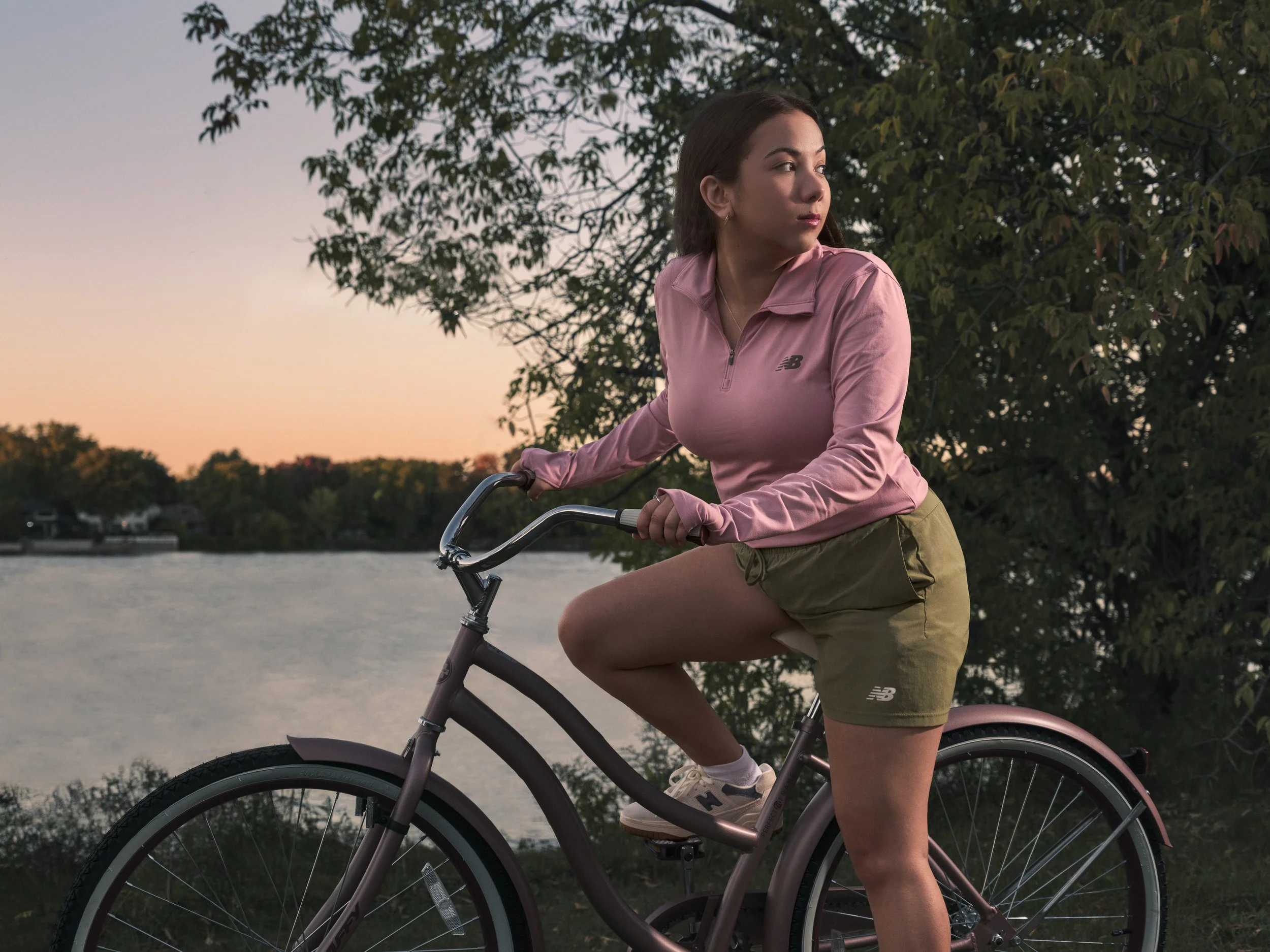 Sportswear campaign image of model seated on bicycle near water at sunset