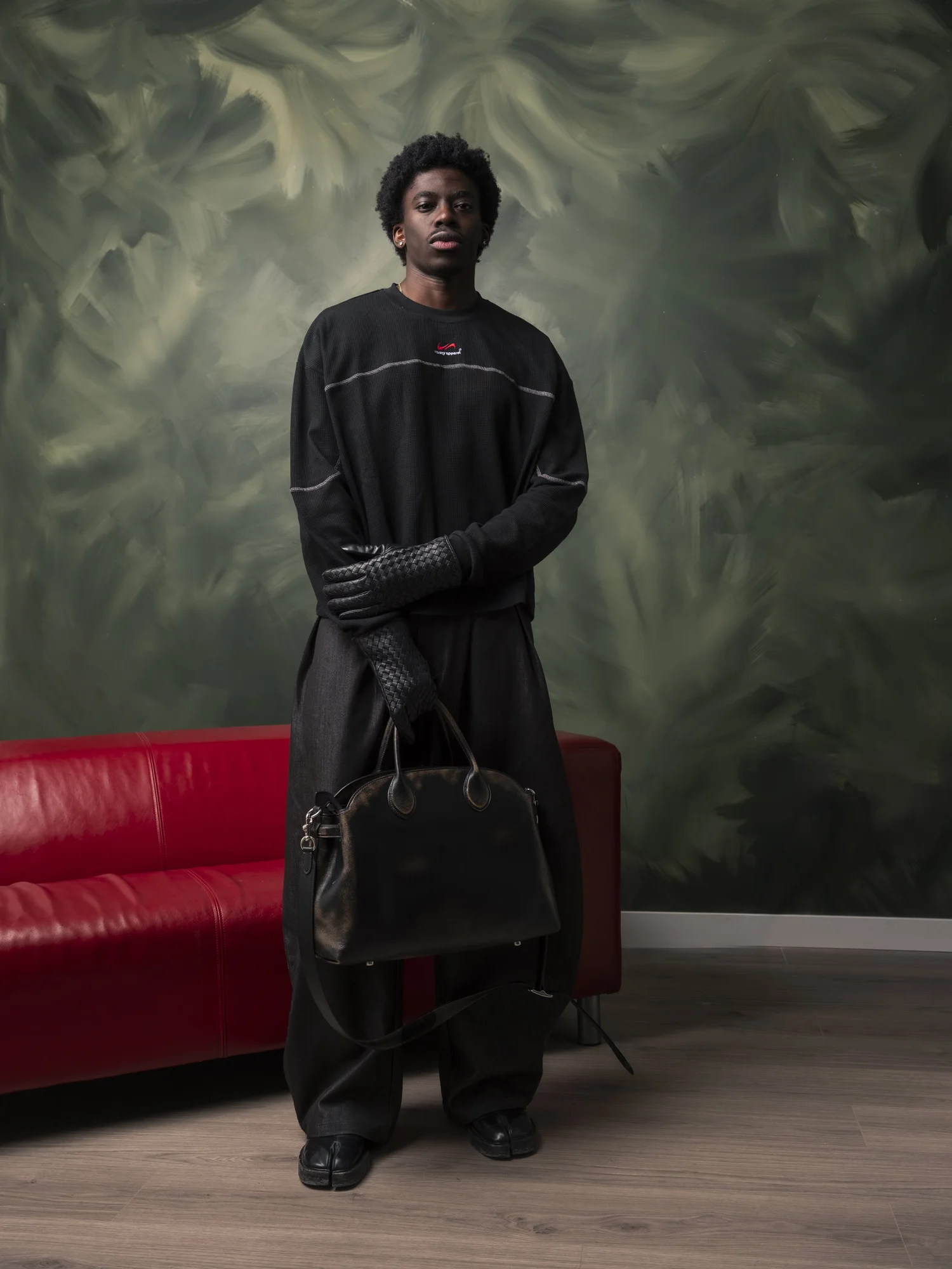 Studio fashion editorial image with model standing beside red sofa and dark green backdrop
