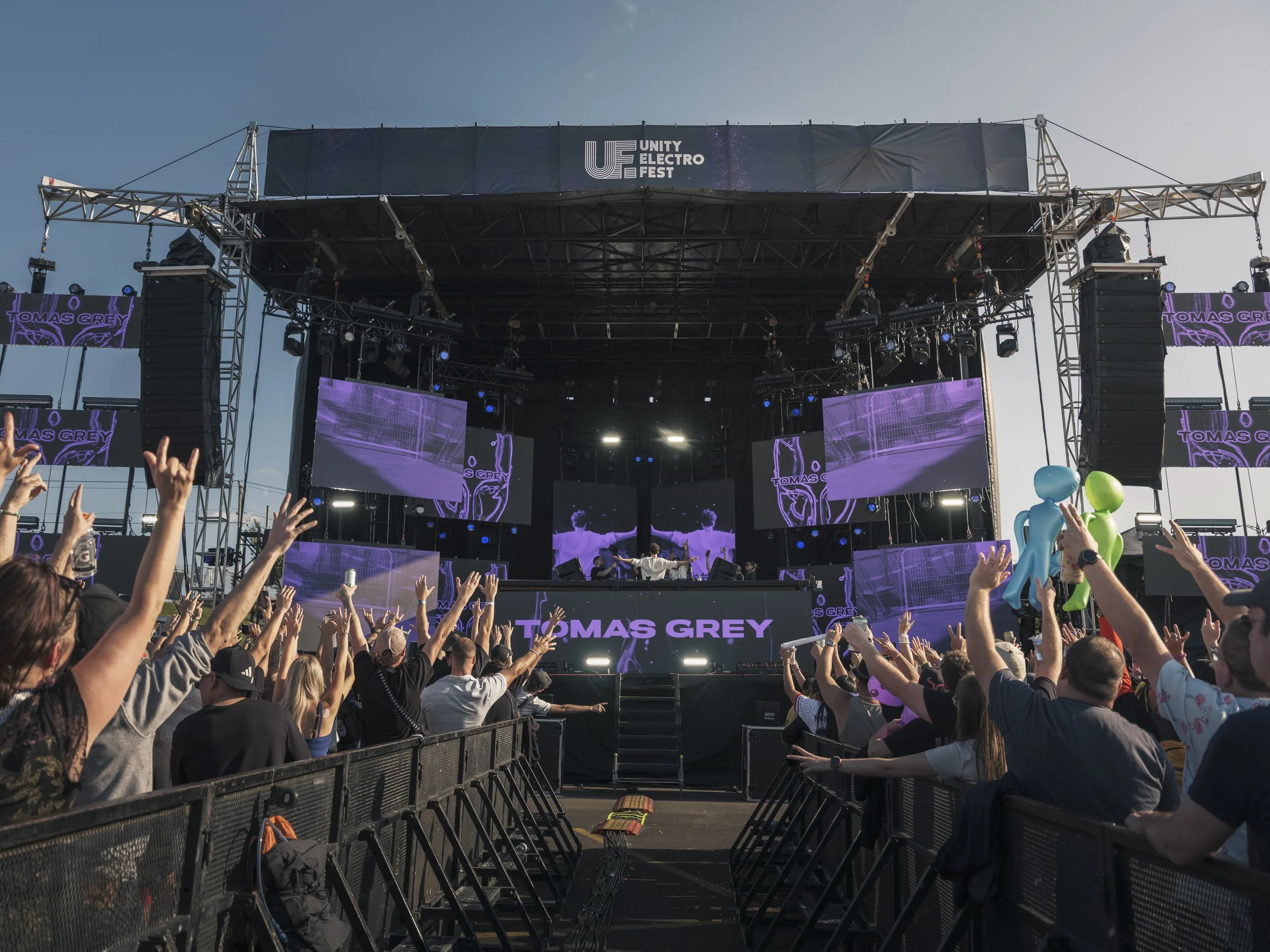 Wide crowd view with purple stage lighting and raised hands during Unity Electrofëst