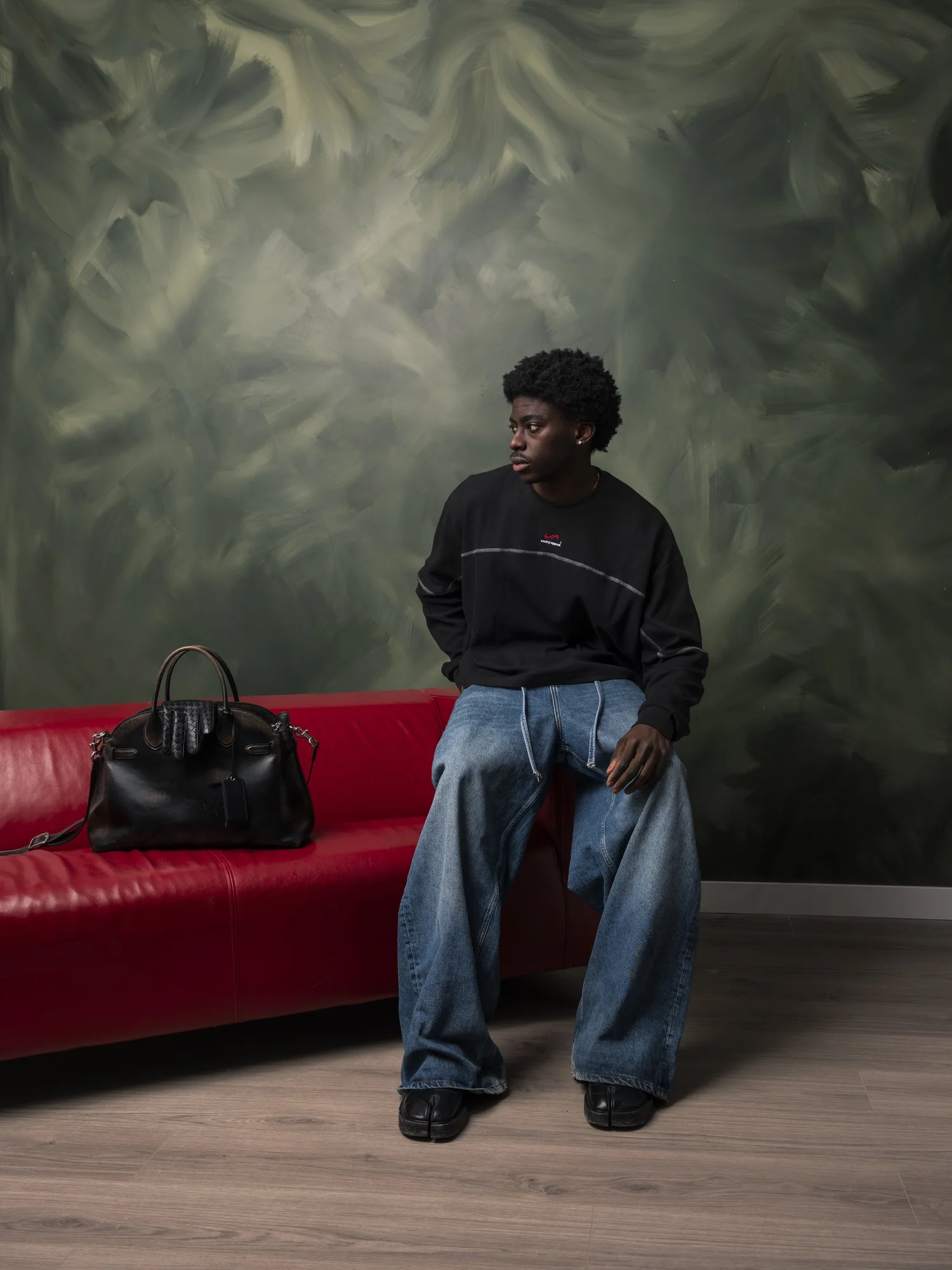 Studio fashion editorial image with seated model in denim near red sofa