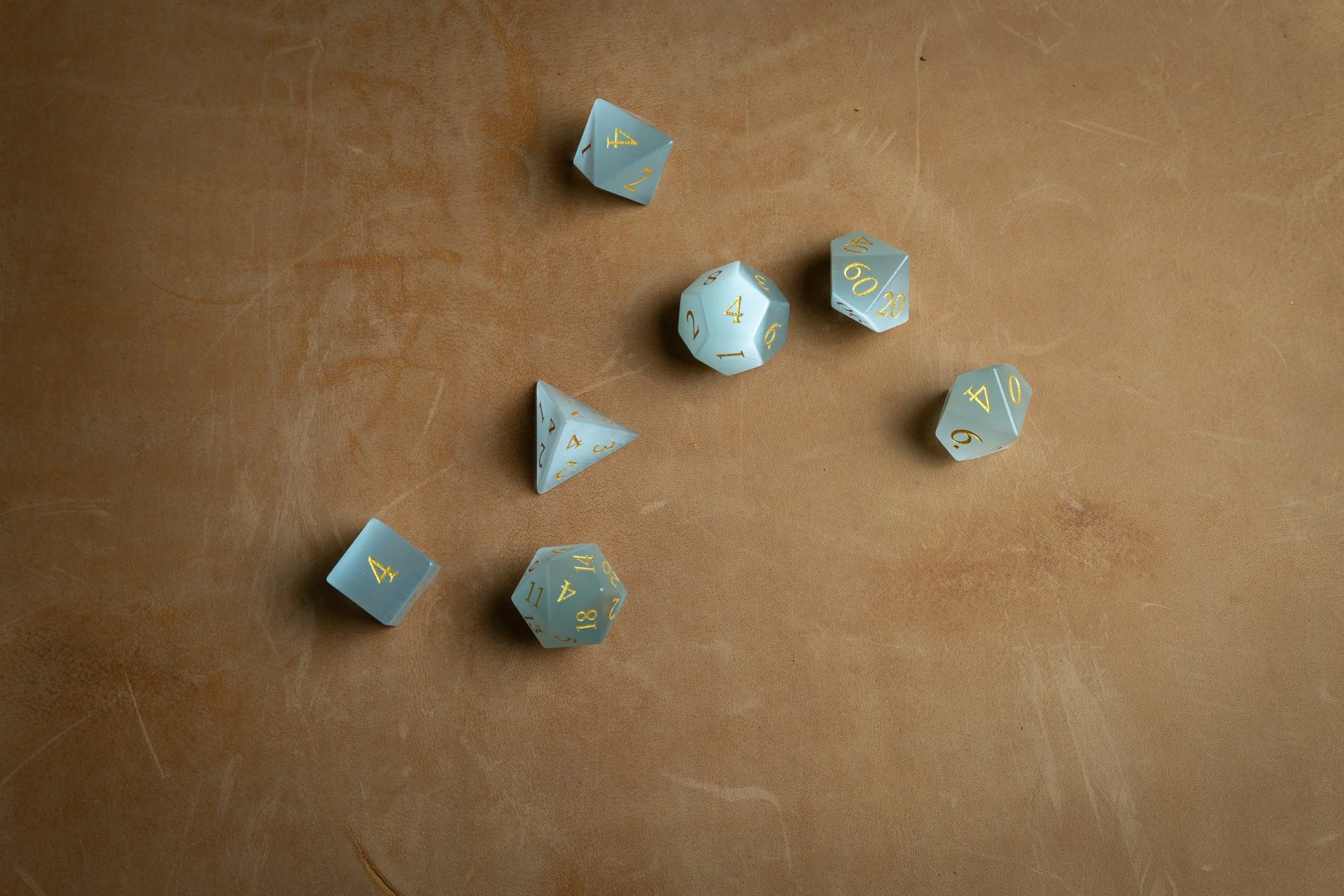 Multiple light blue gemstone dnd gaming dice with gold numbering scattered on a brown surface.
