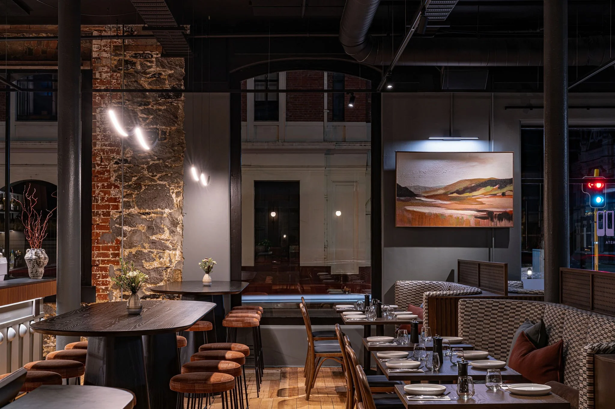 Interior of a modern restaurant with brick and stone walls, contemporary lighting, and neatly set tables with plates and utensils.