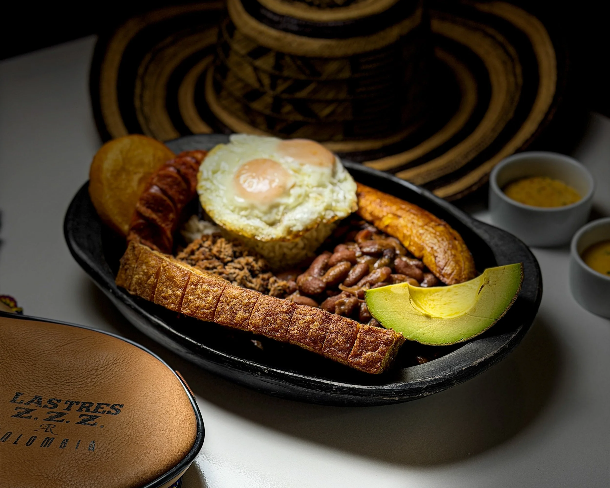 Traditional Mexican breakfast platter with fried eggs, plantains, sausage, beans, avocado, and toast, served on a black plate.
