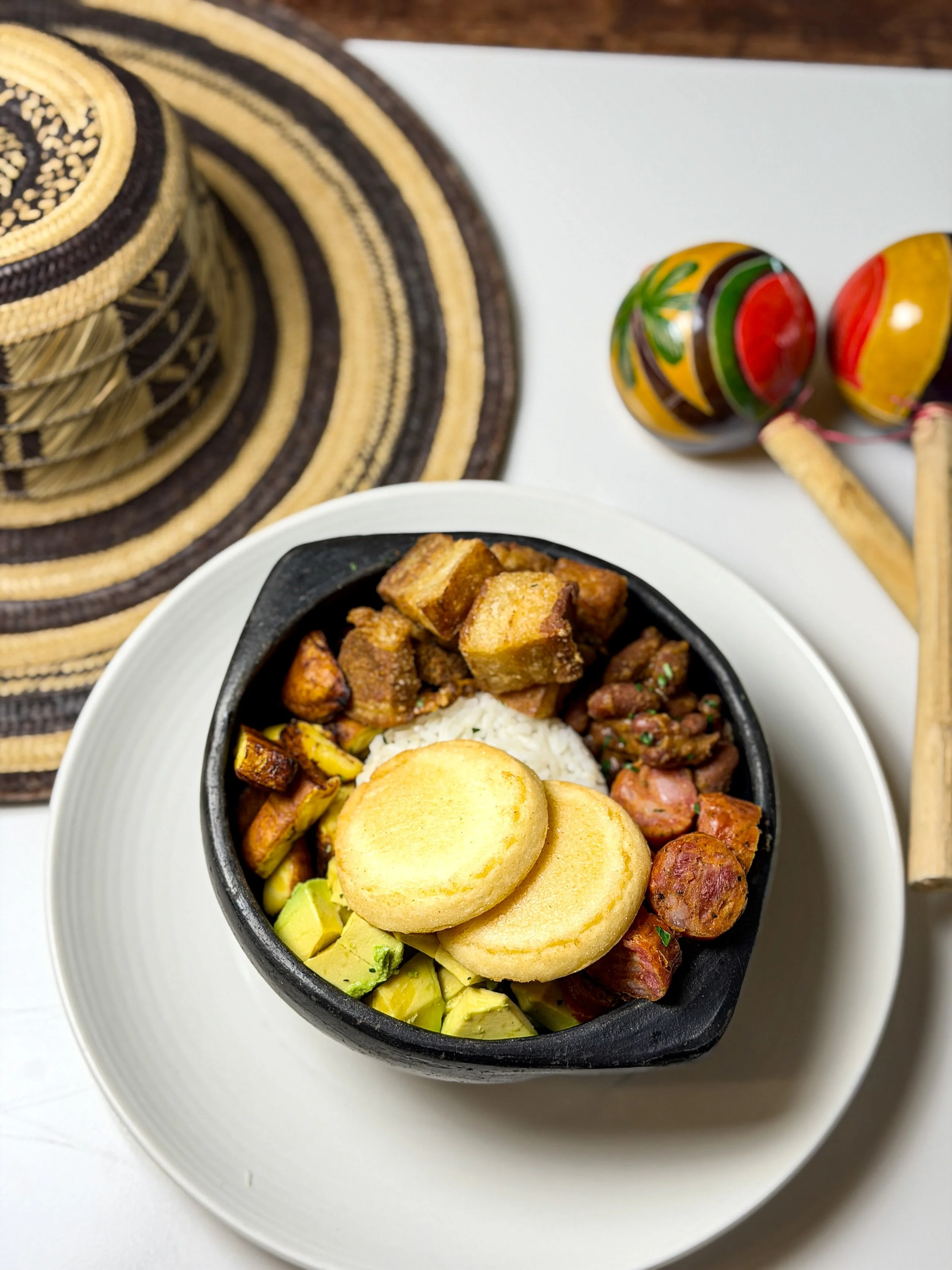 A bowl of Colombian bandeja paisa with rice, fried plantains, avocado, beans, chicharrón, sausage, and pork.