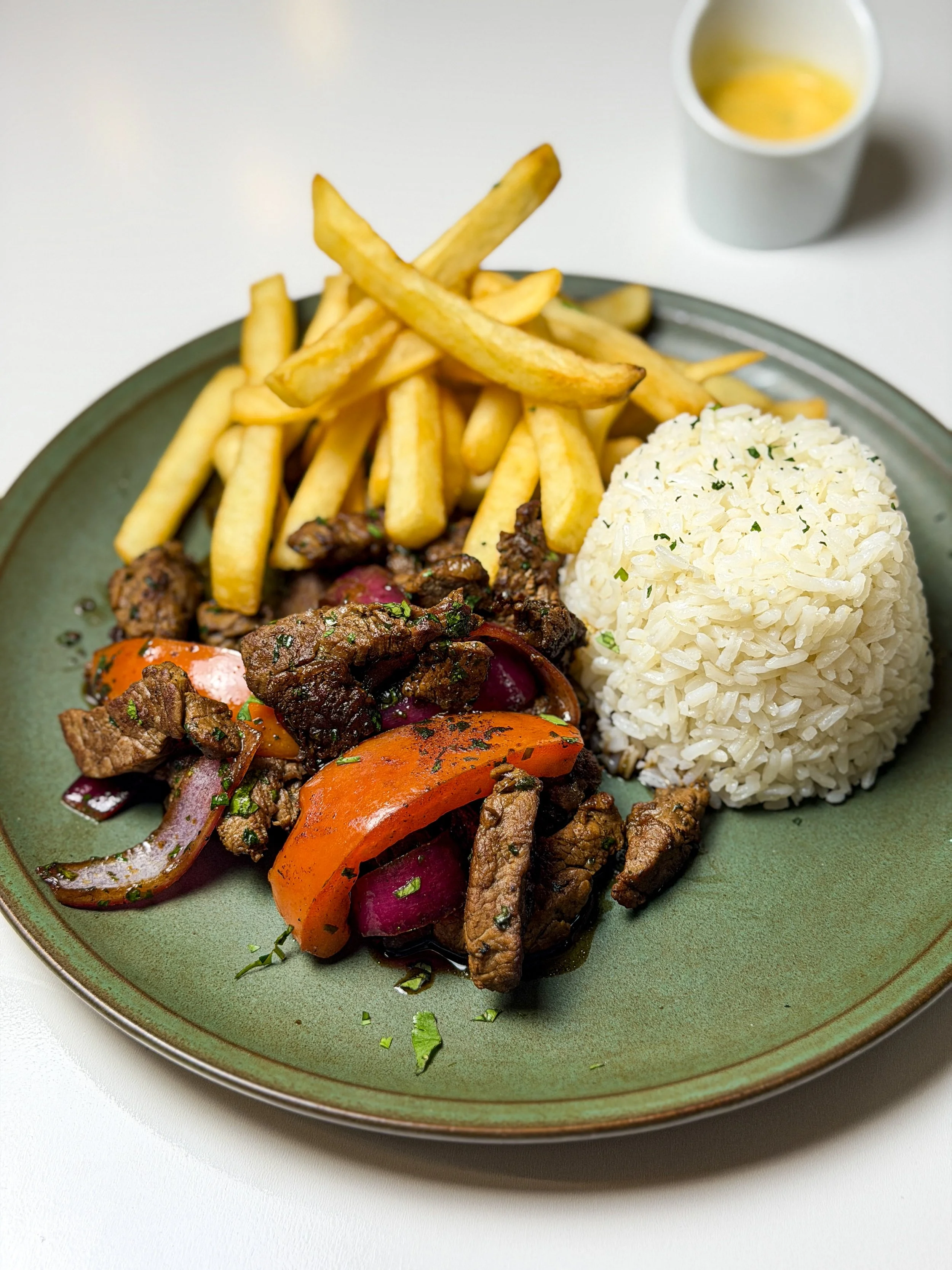 Plate of French fries, a scoop of rice, and a beef stir-fry with vegetables, served with a small cup of dipping sauce.