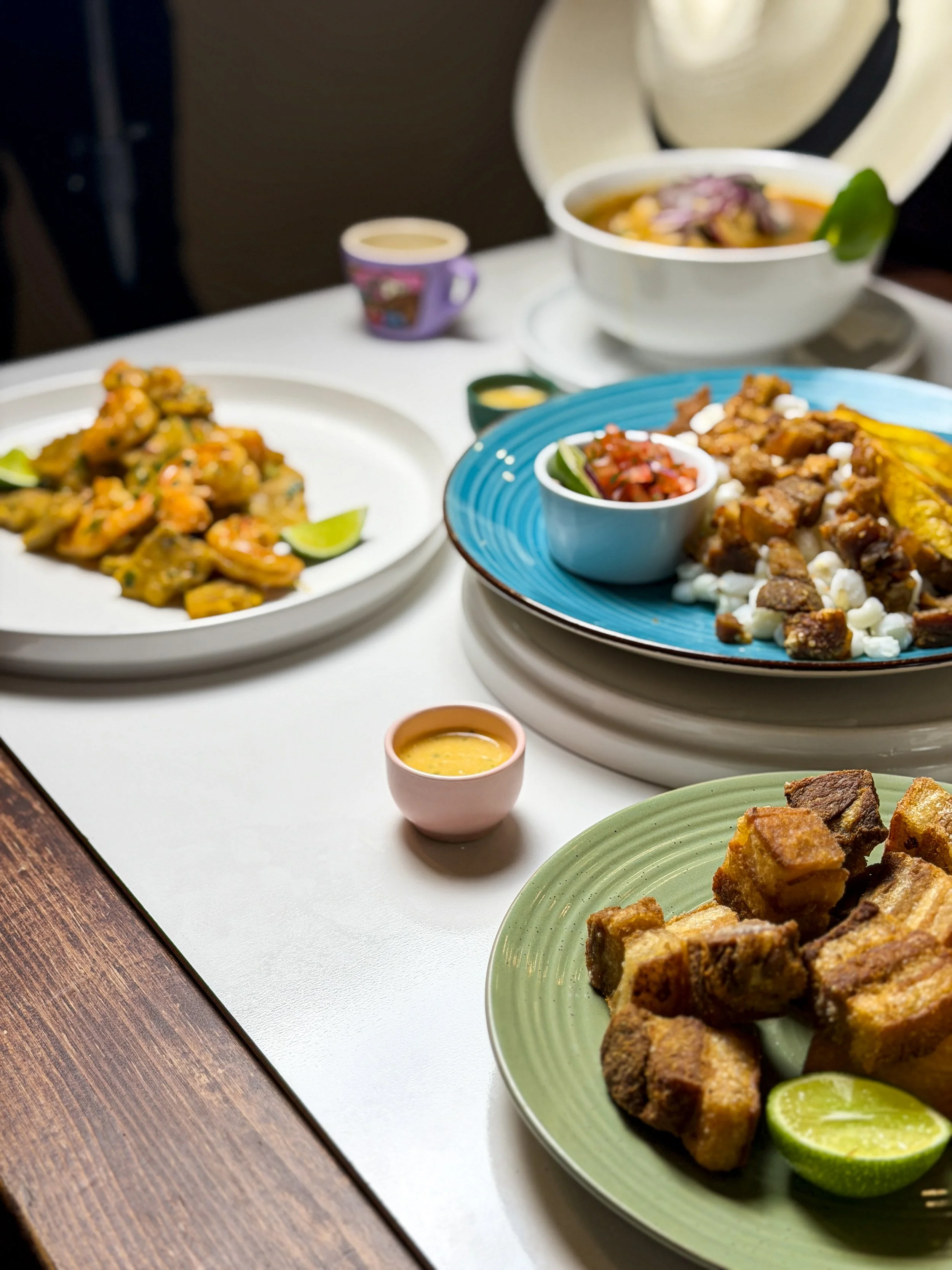 A table with various Mexican dishes including chicharrón, tacos, rice, and salsa, along with lime wedges and small bowls of sauce.
