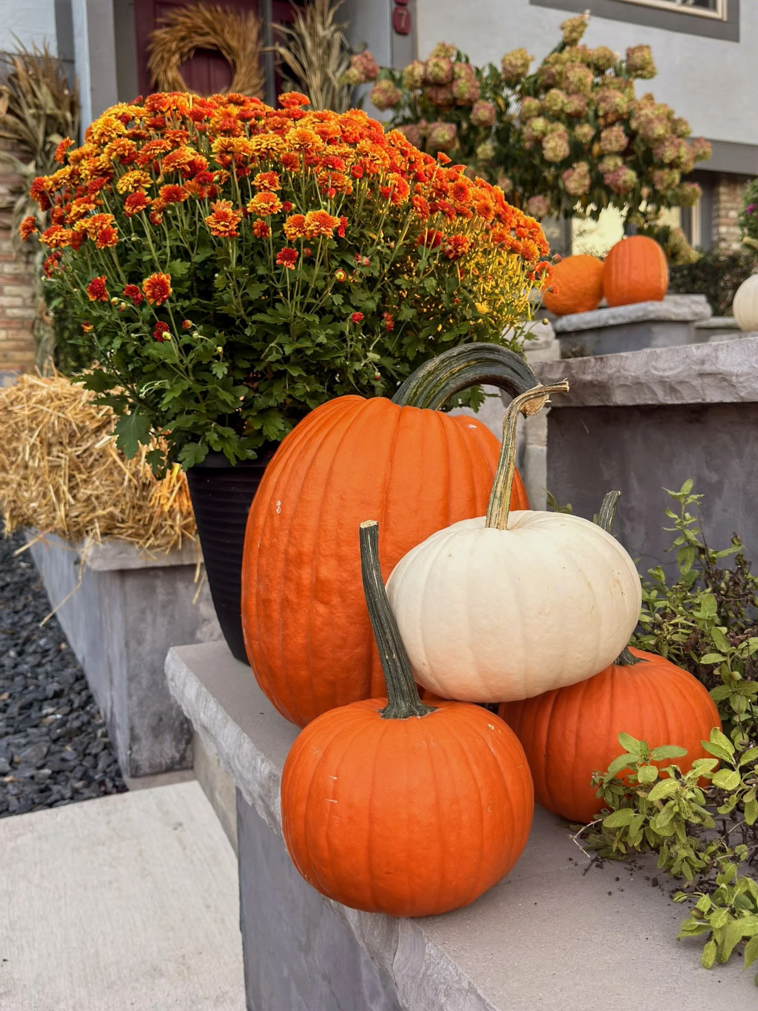 Orange and white pumpkins stacked on a stone porch step beside a hay bale