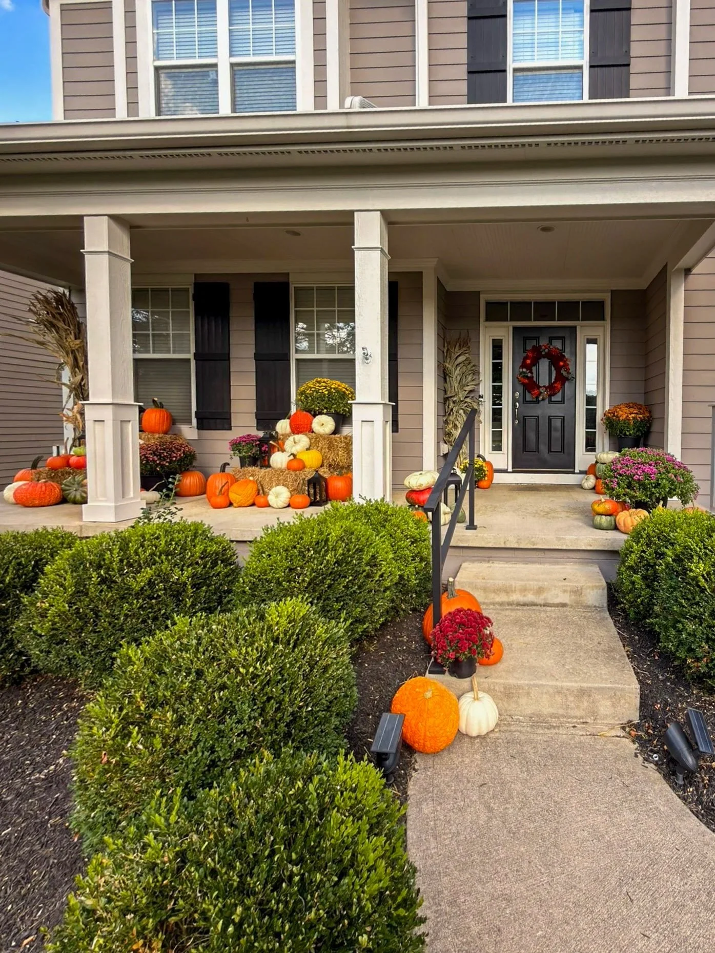 Front porch styled for fall in Columbus with corn stalks, mums and a red wreath on the door