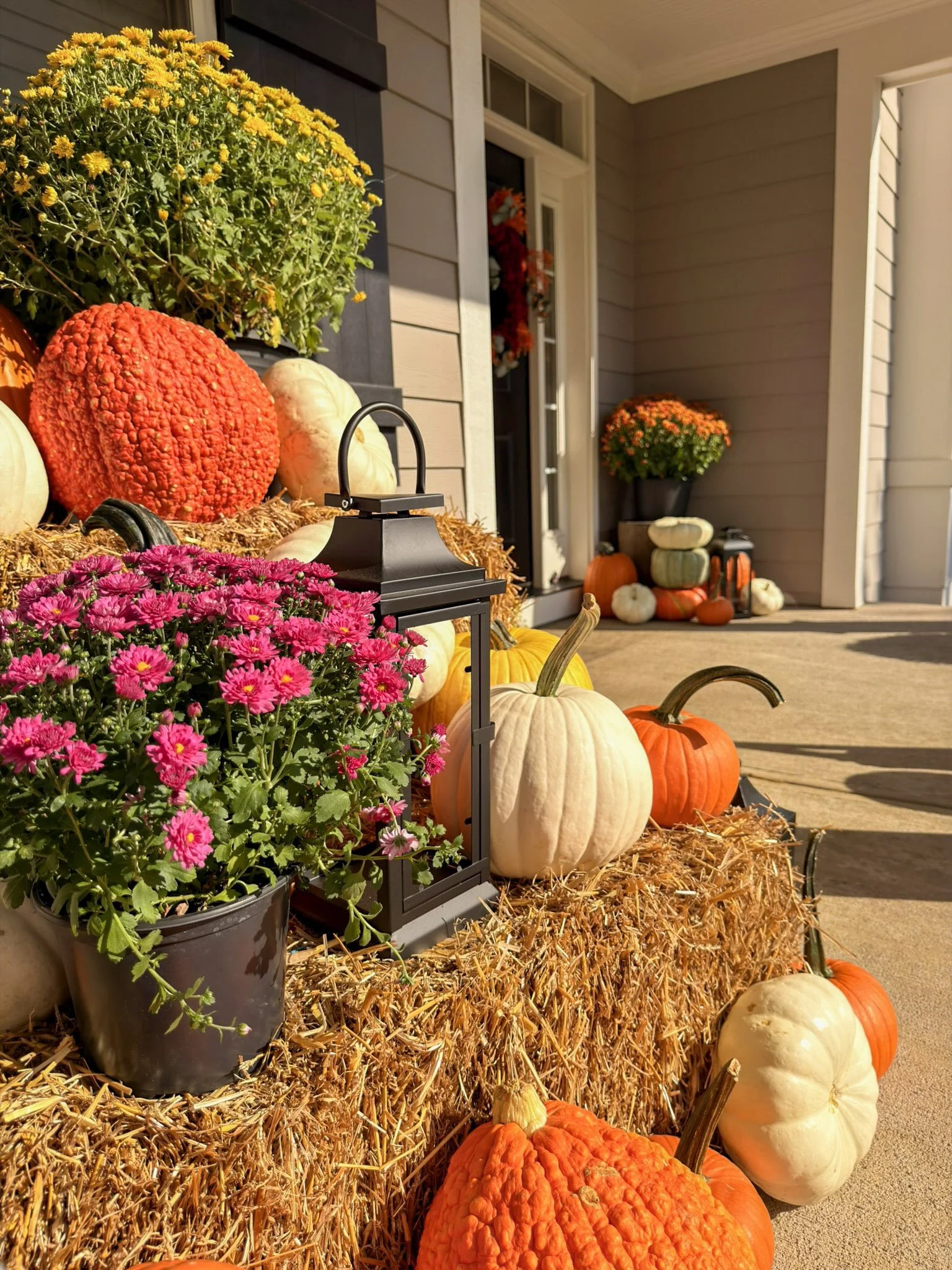 Pink mums, a black lantern and white and orange pumpkins staged on stacked hay bales