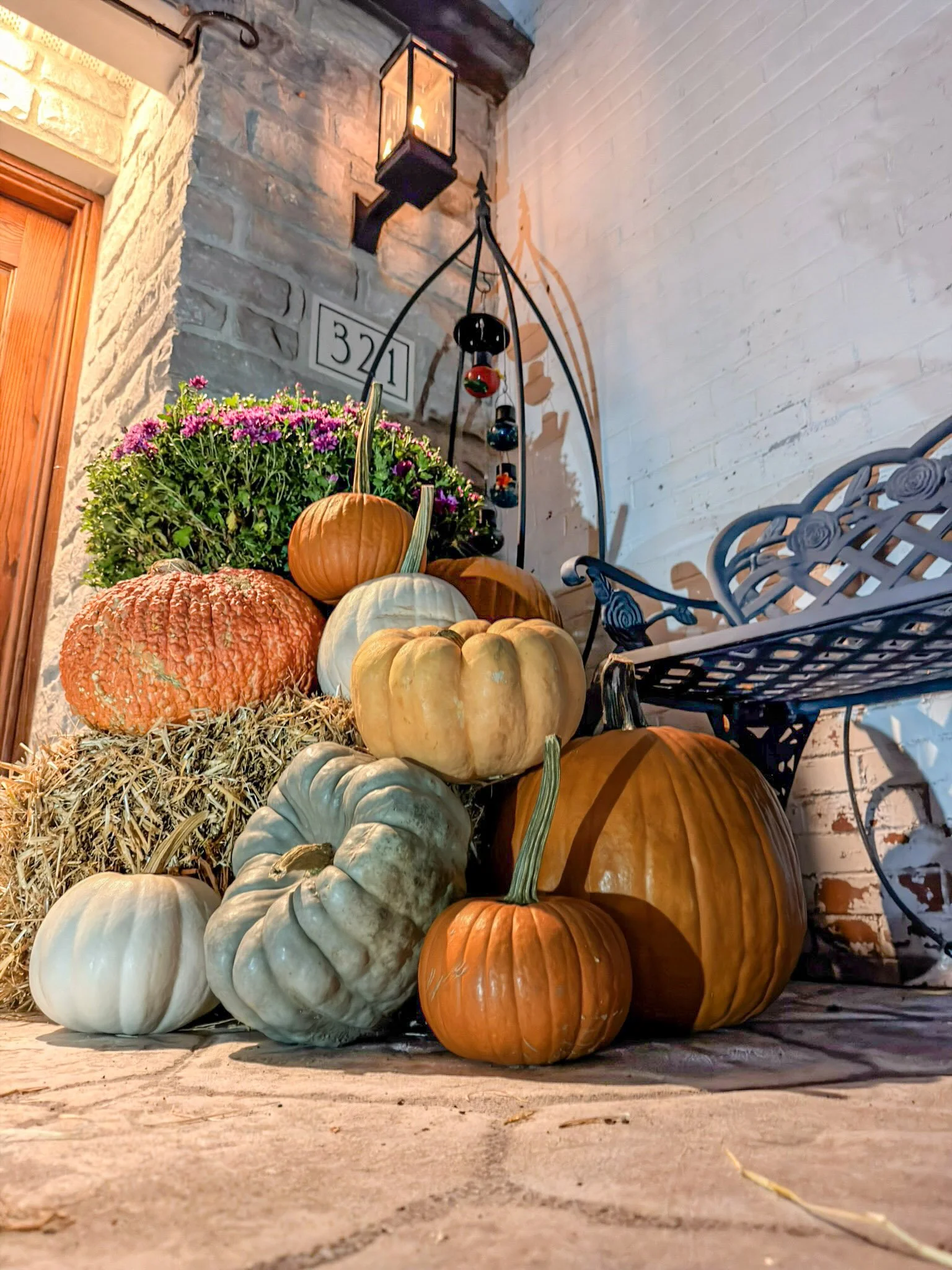 Purple mums, hay bales and a mound of orange and blue green heirloom pumpkins beside a stone entry