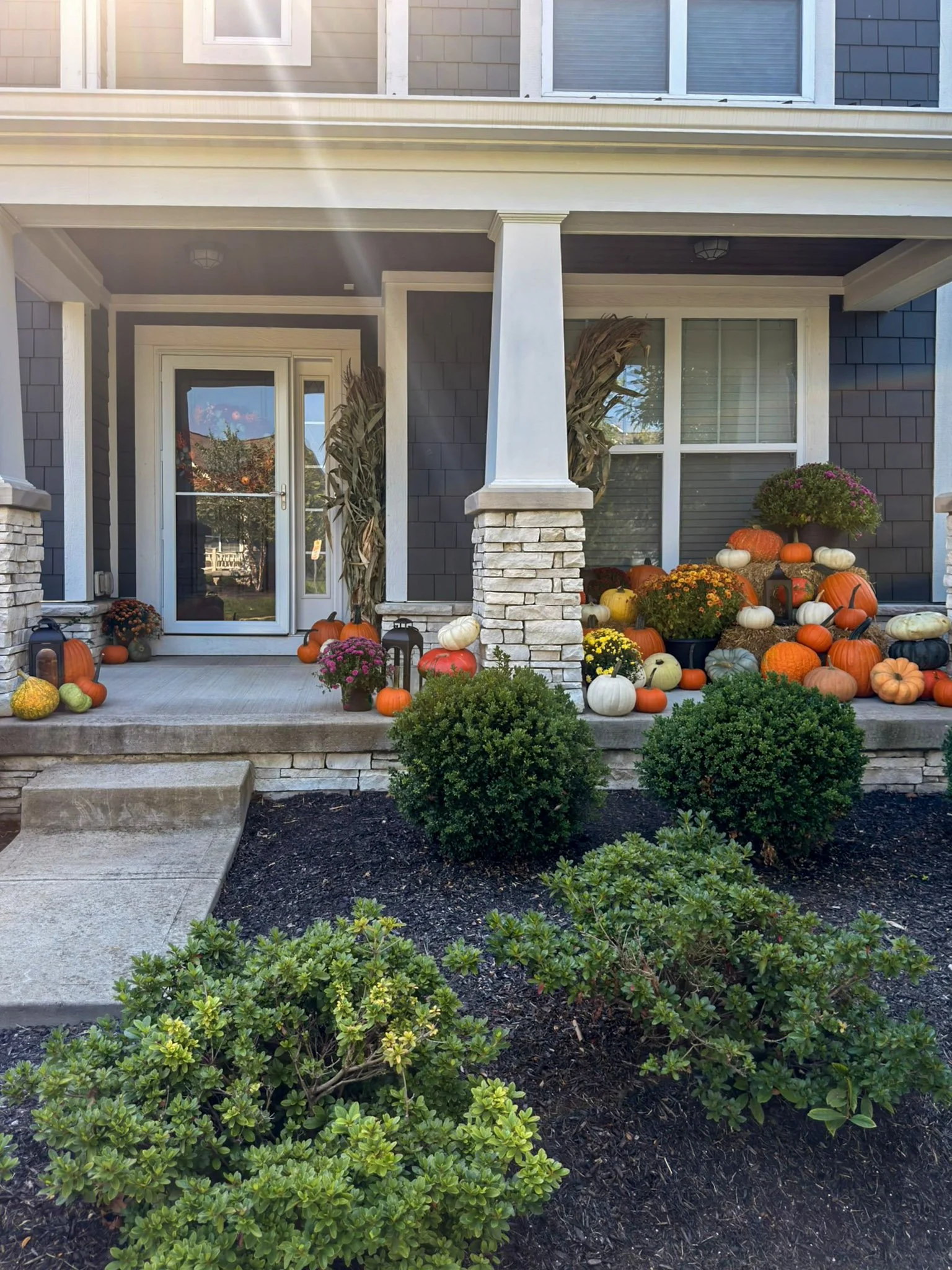 Covered craftsman porch with stone columns and pumpkins lining the porch edge and front steps