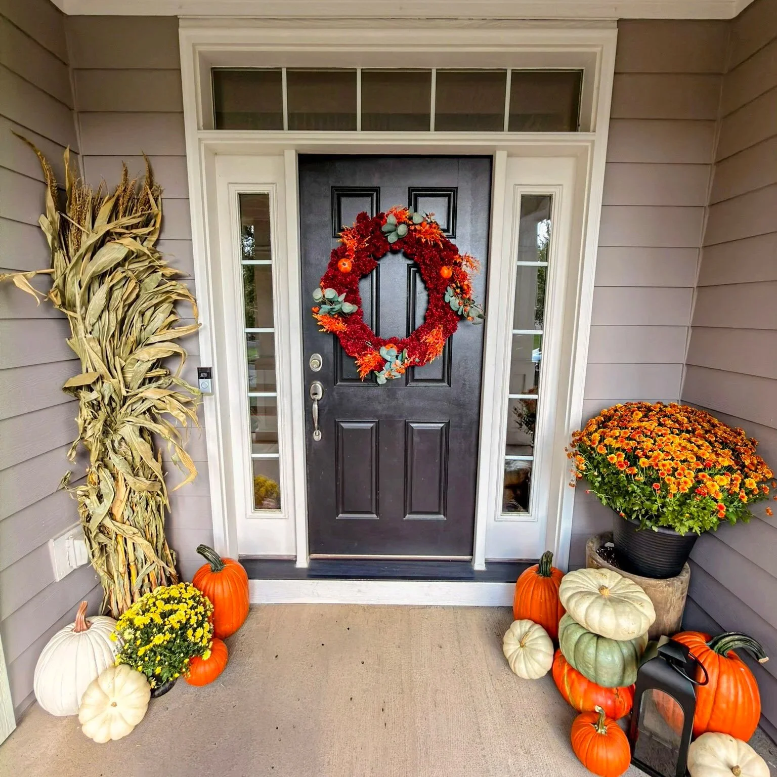Dark front door with a red fall wreath, corn stalks, mums and pumpkins on a covered Columbus porch