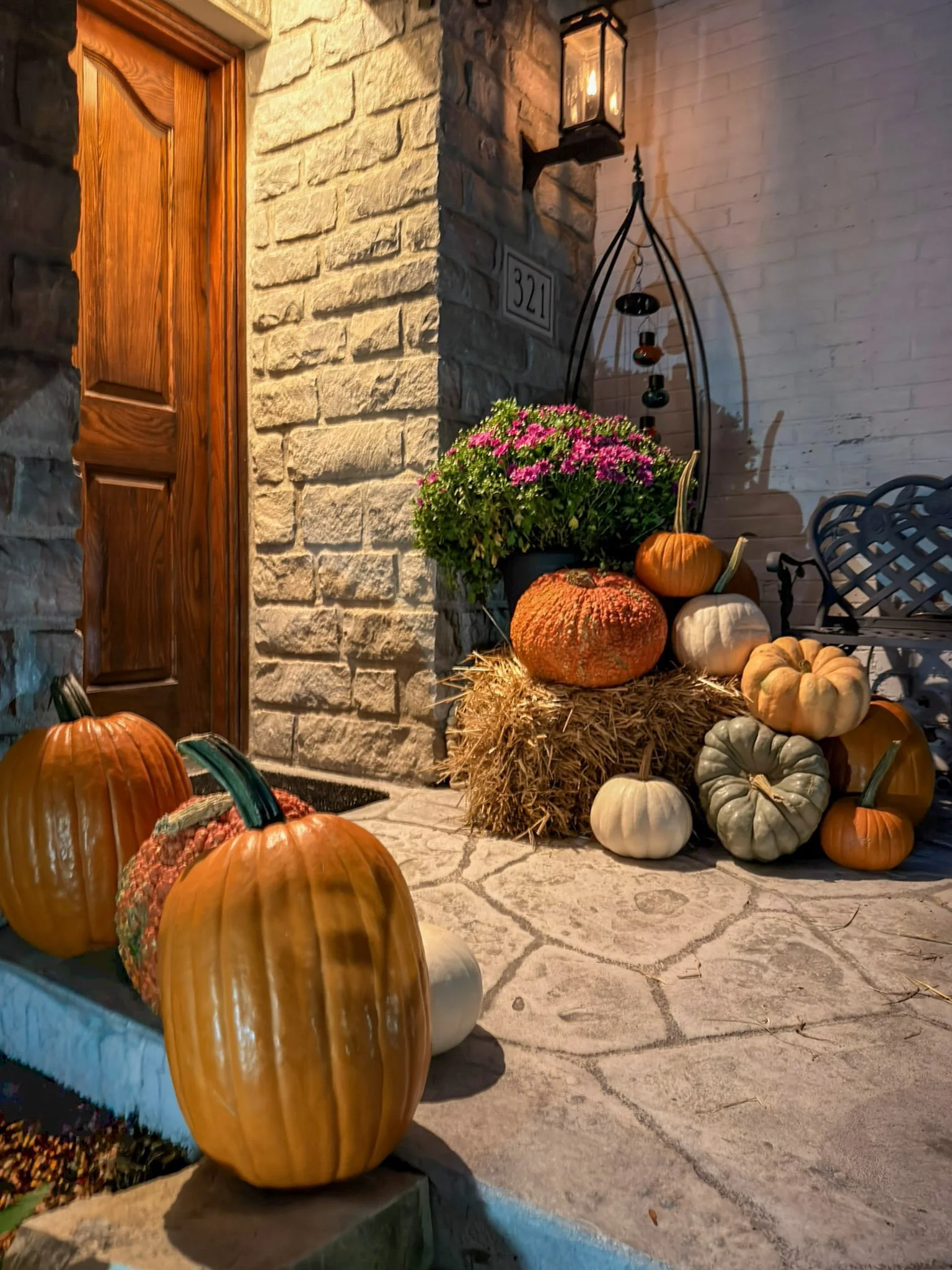 Close view of a large orange pumpkin, hay bale and heirloom white and green pumpkins by a wood front door