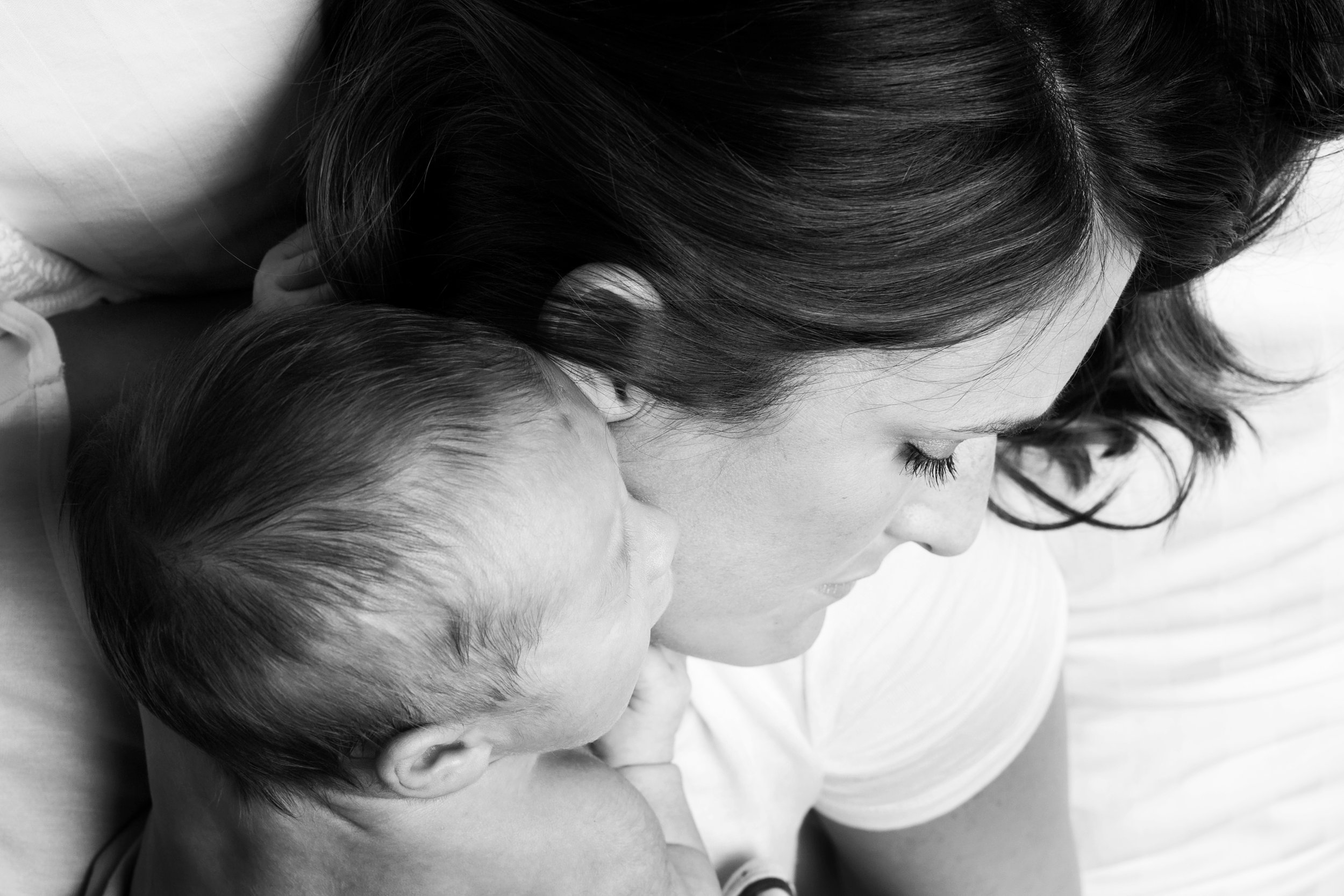 Black and white photo of a mother holding her newborn baby close, with their faces touching, both with eyes closed.