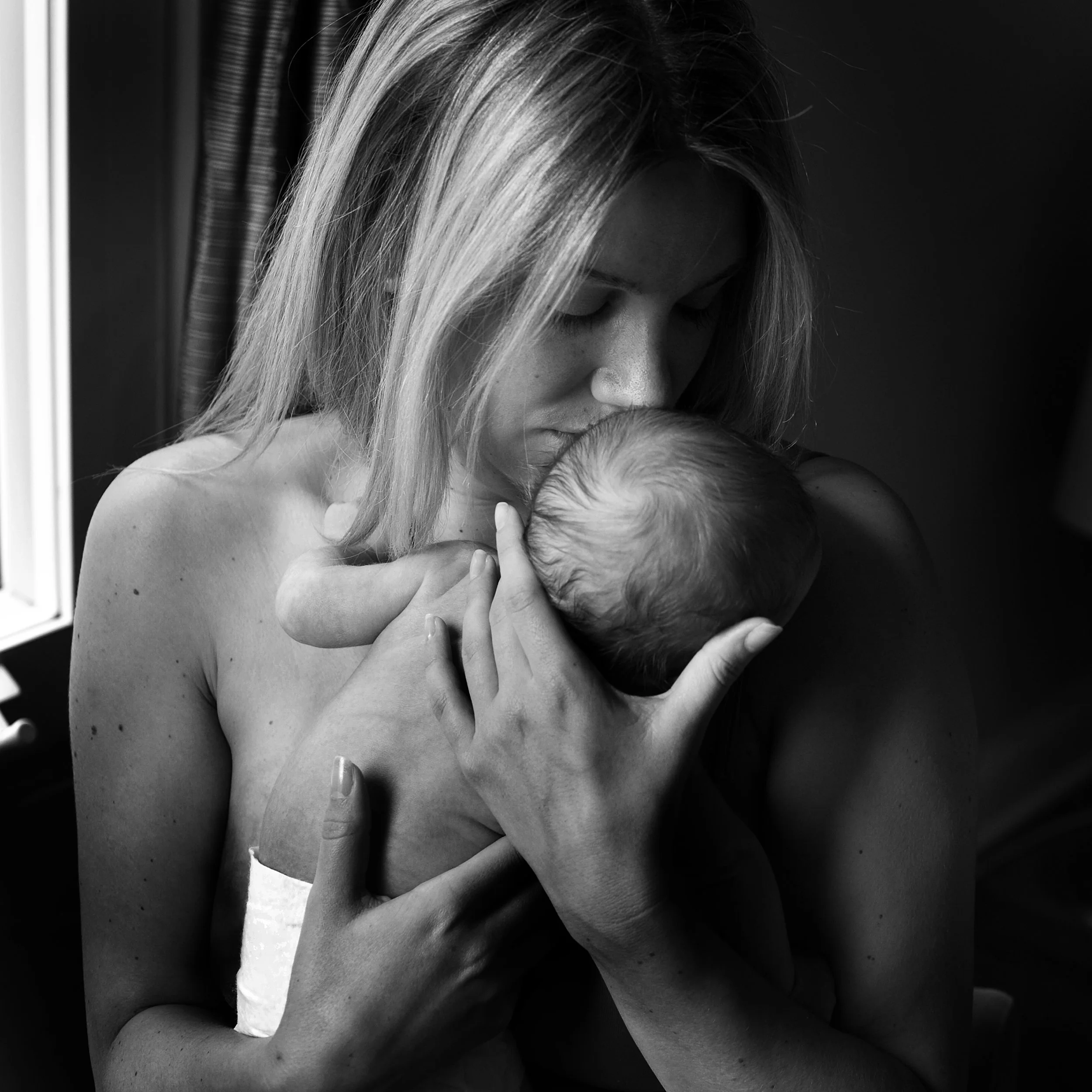 A woman gently holding and kissing a newborn baby close to her chest.