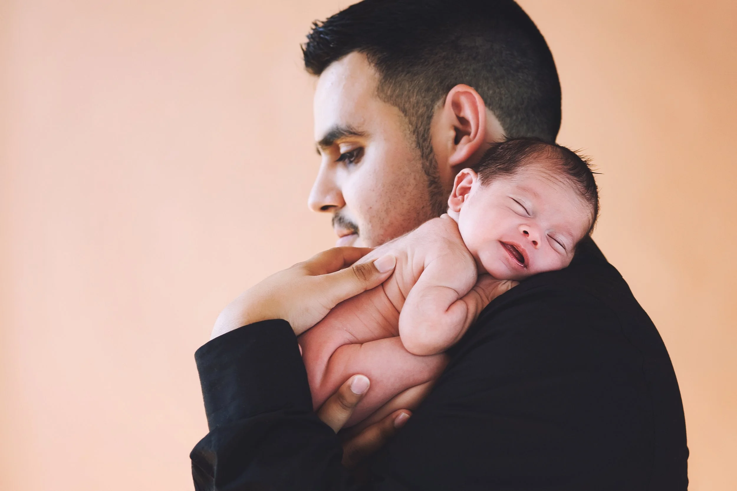 A man holding a smiling baby against a beige background.