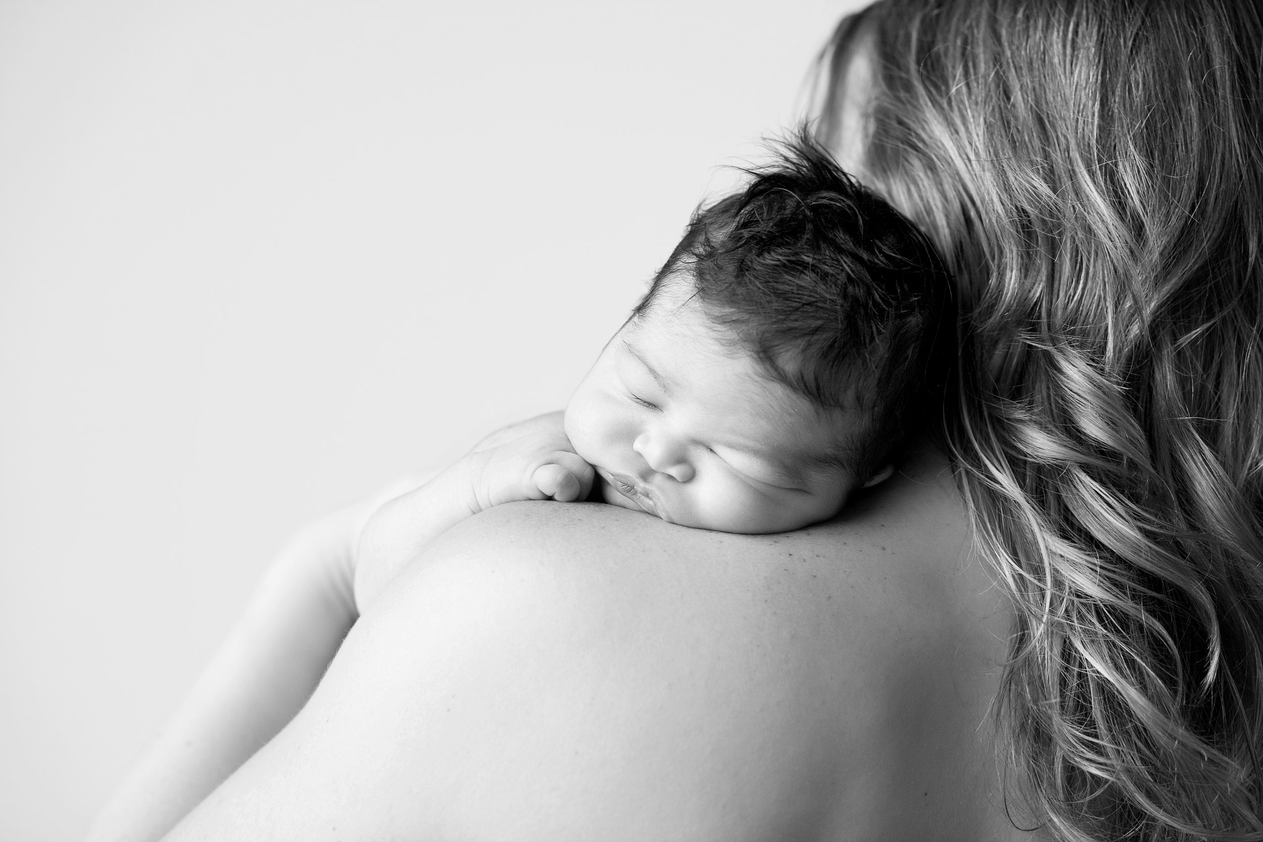 A black and white photo of a newborn baby sleeping on their mother's shoulder.