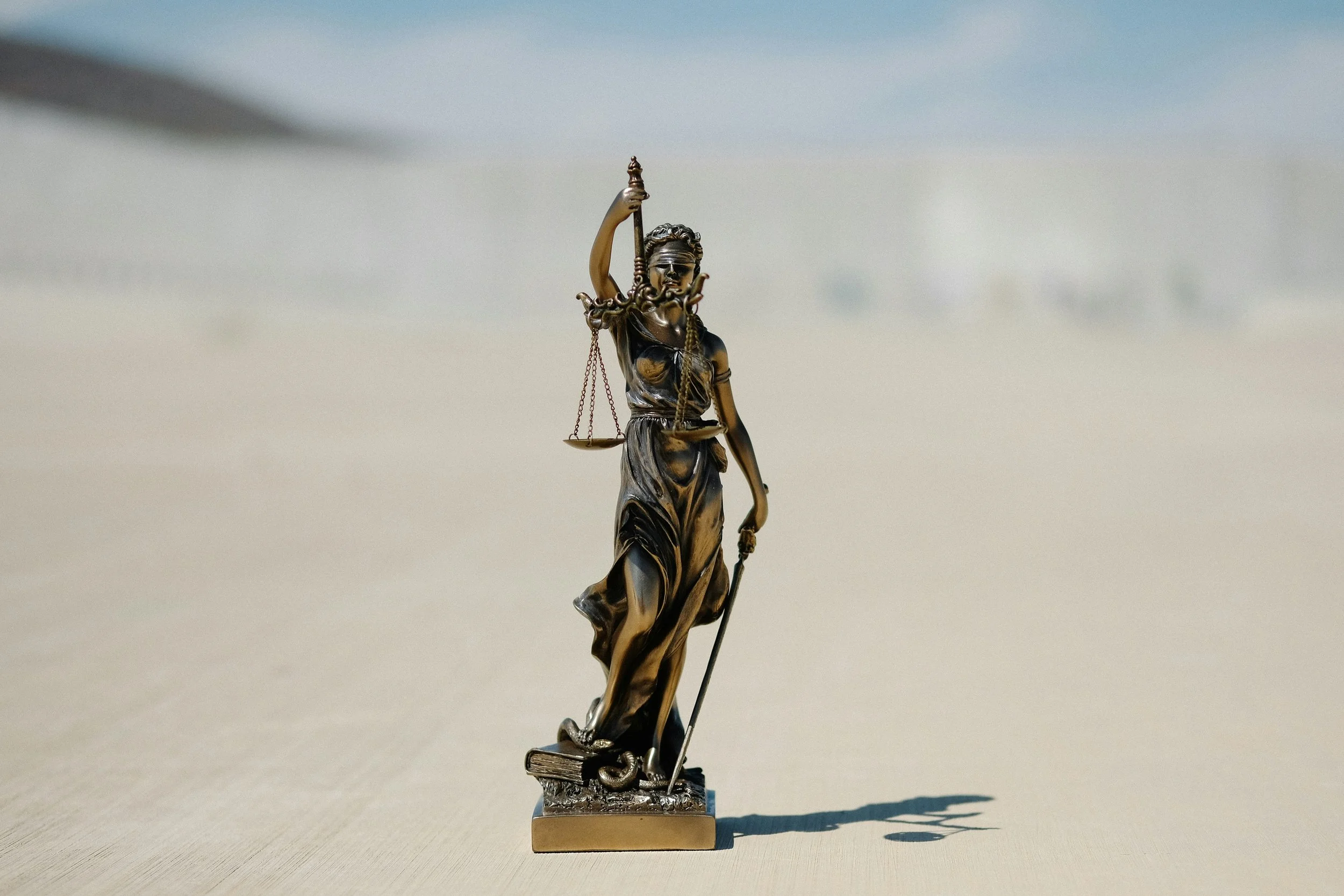 A small metallic statue of Lady Justice holding a sword in her right hand and scales in her left hand, standing on a rectangular base.
