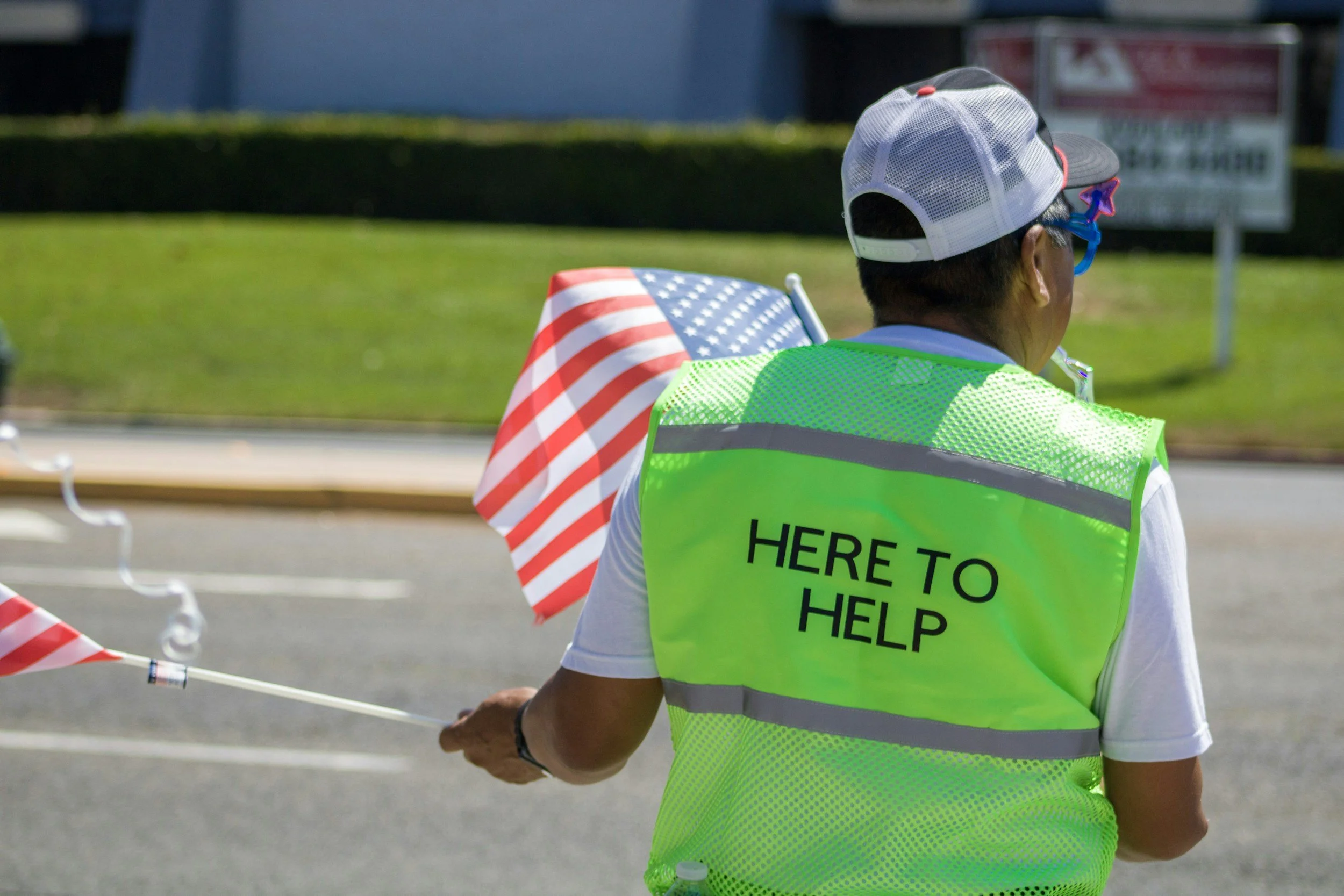 A volunteer holds an American flag and wears a safety vest that reads here to help