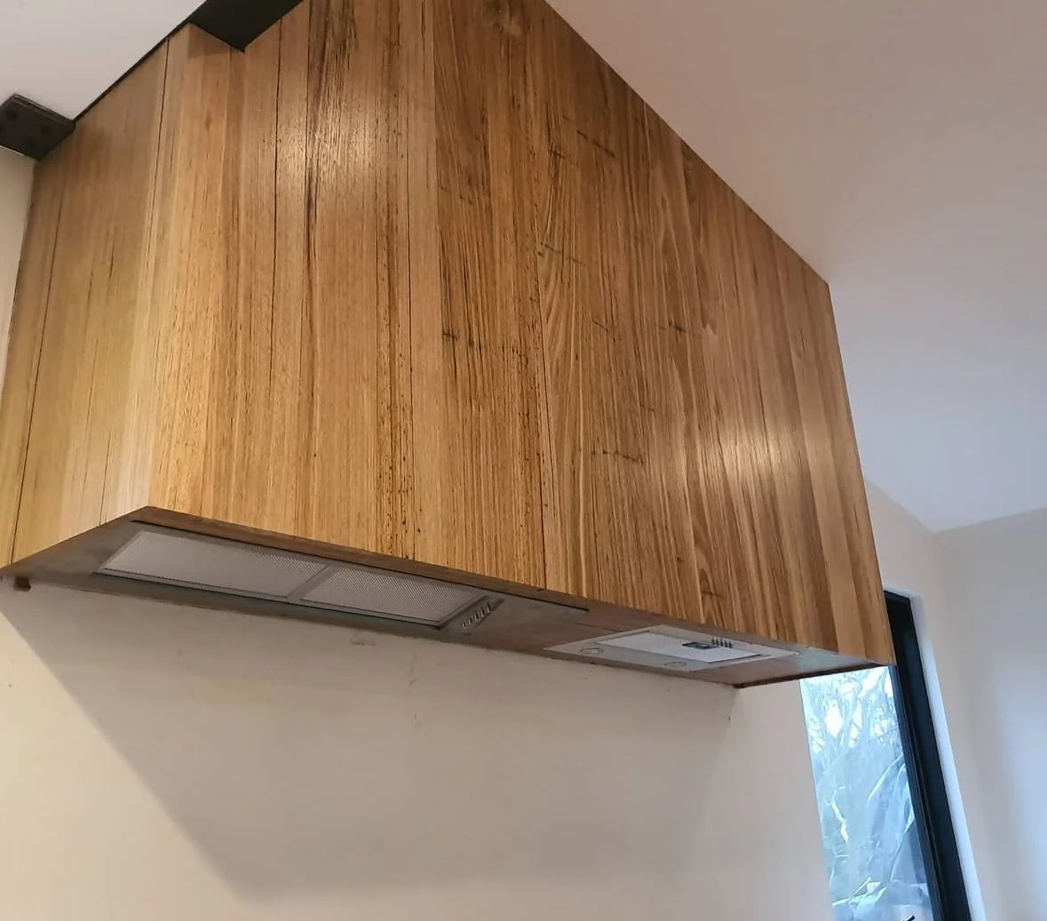 Wooden kitchen cabinet mounted on a wall above a range hood, next to a window.