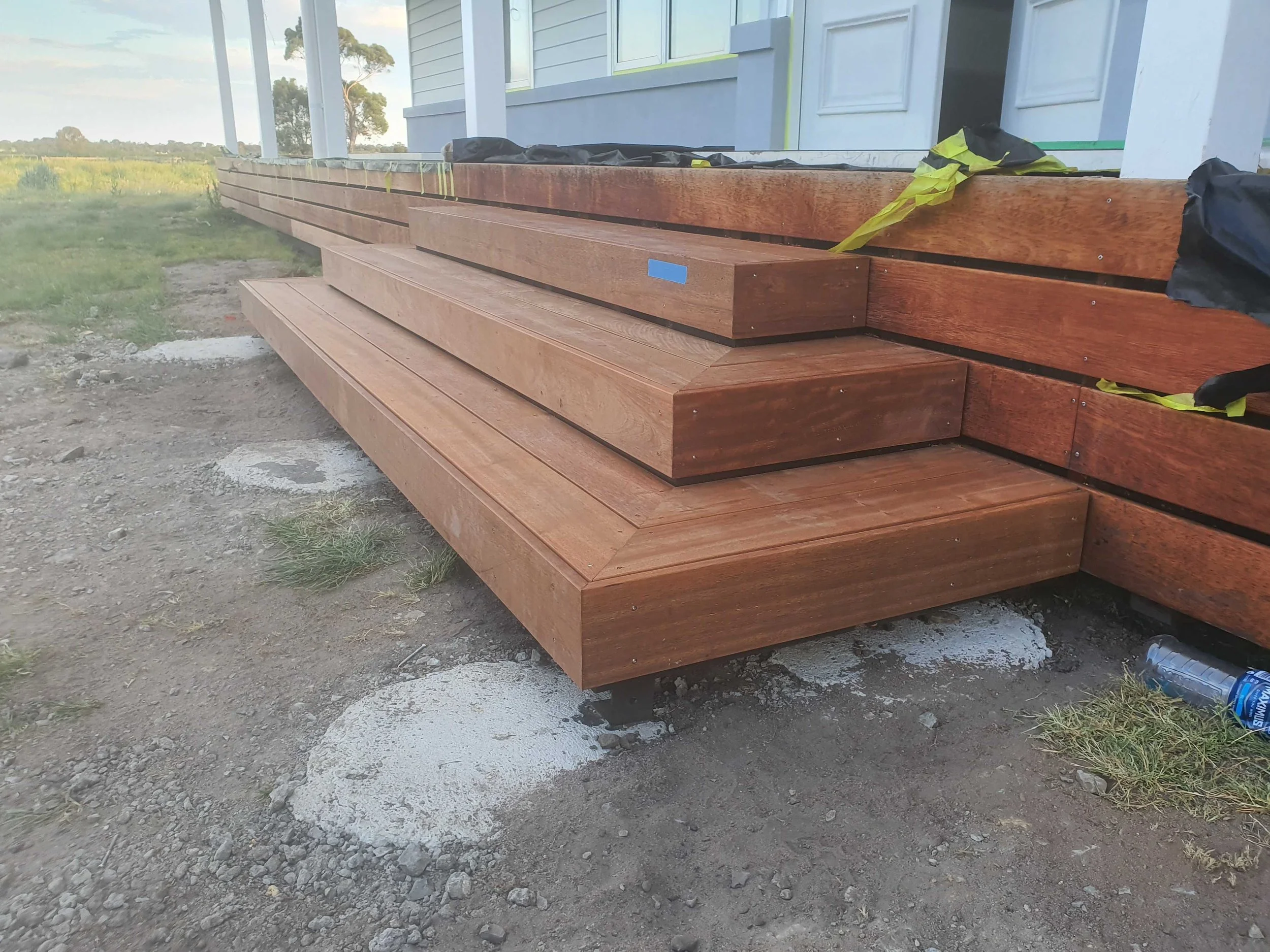 Wooden stairs being installed on a house porch, with some construction materials and tools nearby.