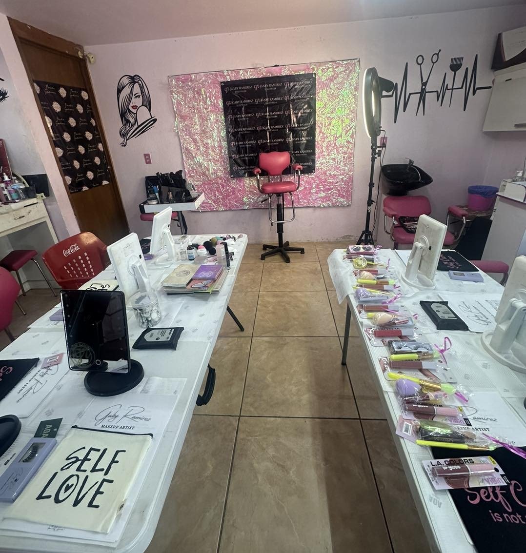 Beauty salon with makeup stations, pink chairs, and hair styling equipment, decorated with artwork and promotional materials.