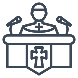 A person dressed as a priest speaking at a podium with microphones.