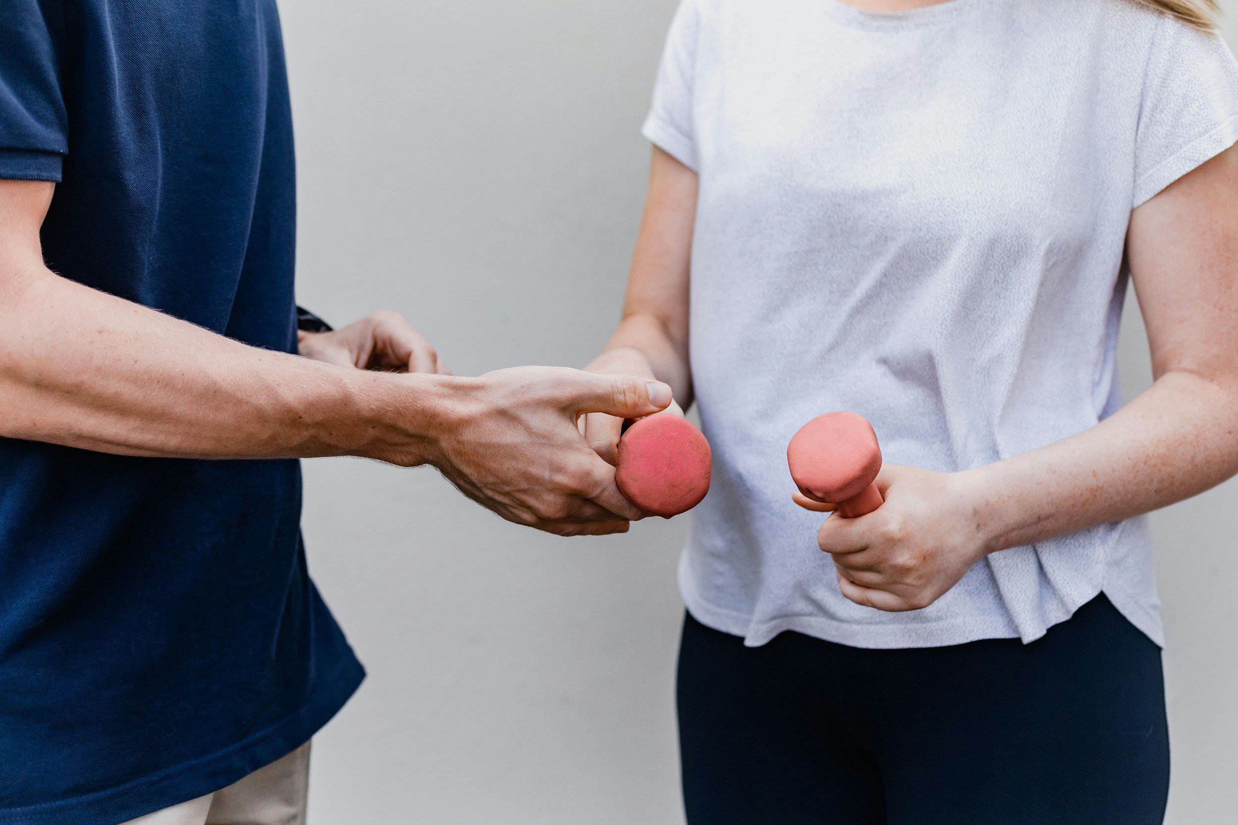 Two women exchanging pink rubber massage balls, standing close to each other.
