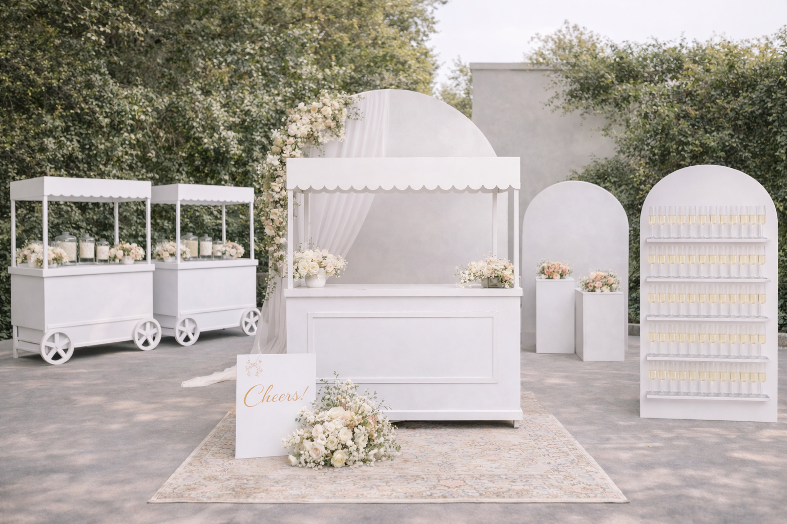 Elegant outdoor wedding bar setup with white furniture, floral arrangements, and champagne glasses, decorated with a 'Cheers!' sign.