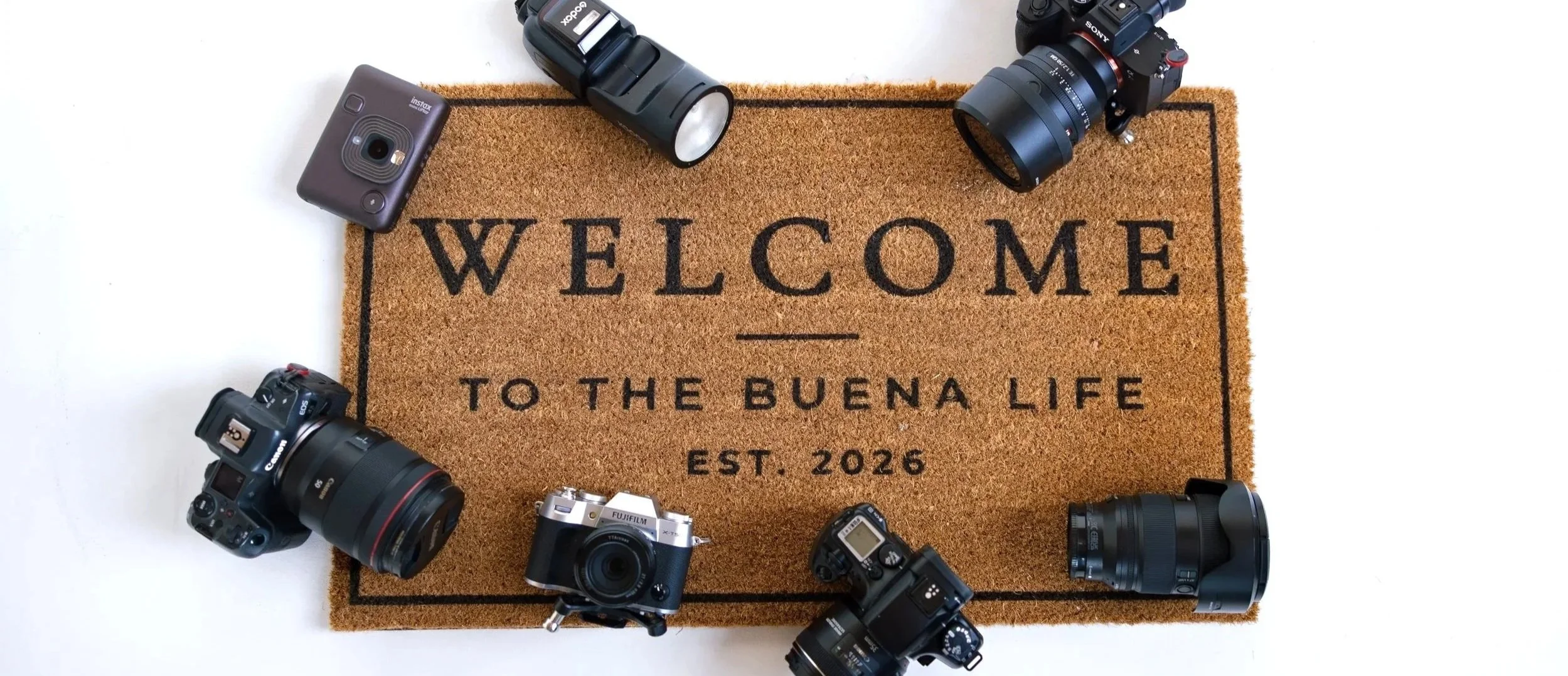 A welcome mat surrounded by cameras and photography equipment.