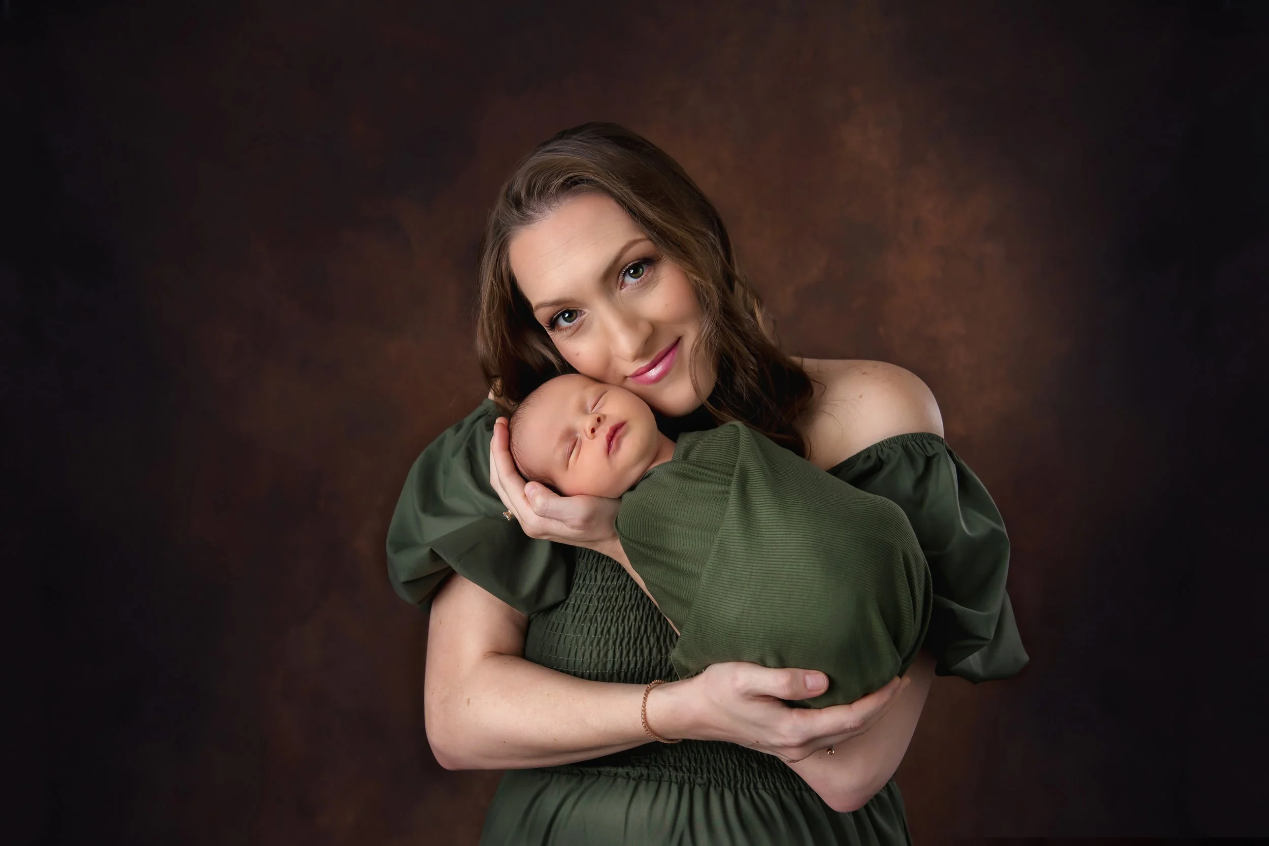A woman holding a sleeping baby against a brown textured background.