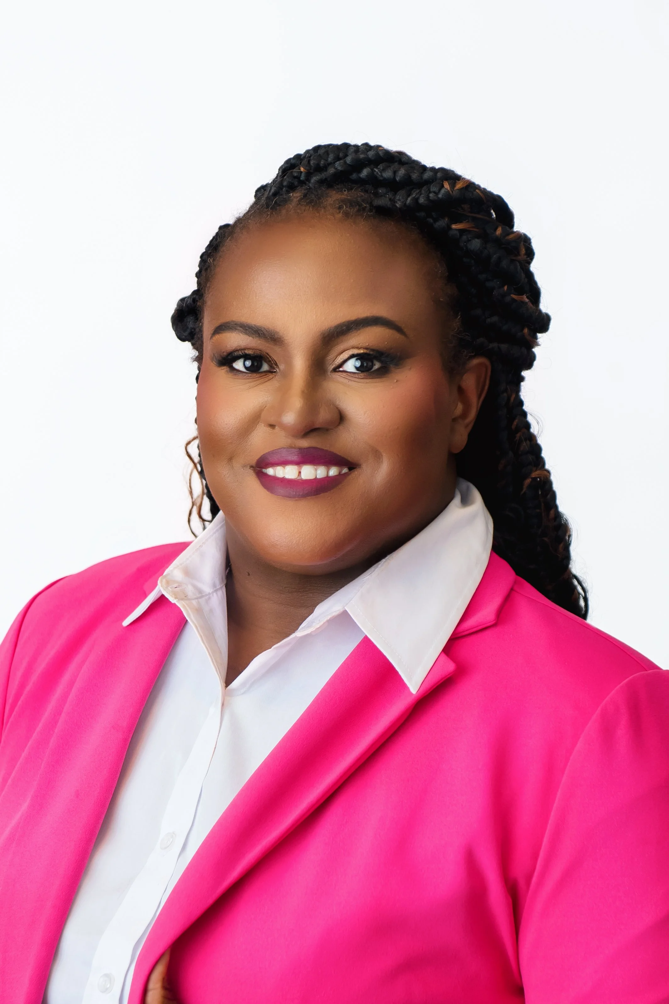 A smiling woman with dark braids wearing a pink blazer and white shirt against a white background in our Spring Branch studio.