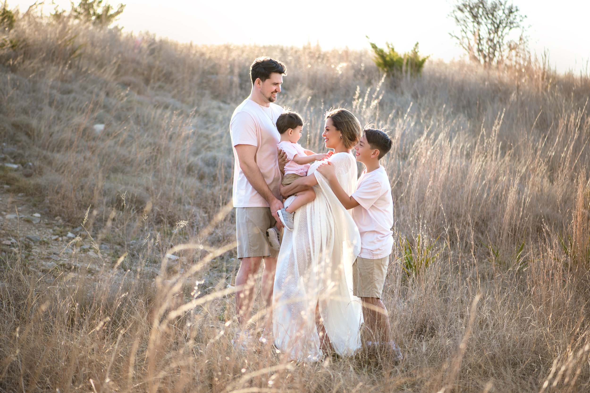 Luxury family portrait of five standing together in tall grass at sunset in the Texas Hill Country, captured for a timeless heirloom experience.