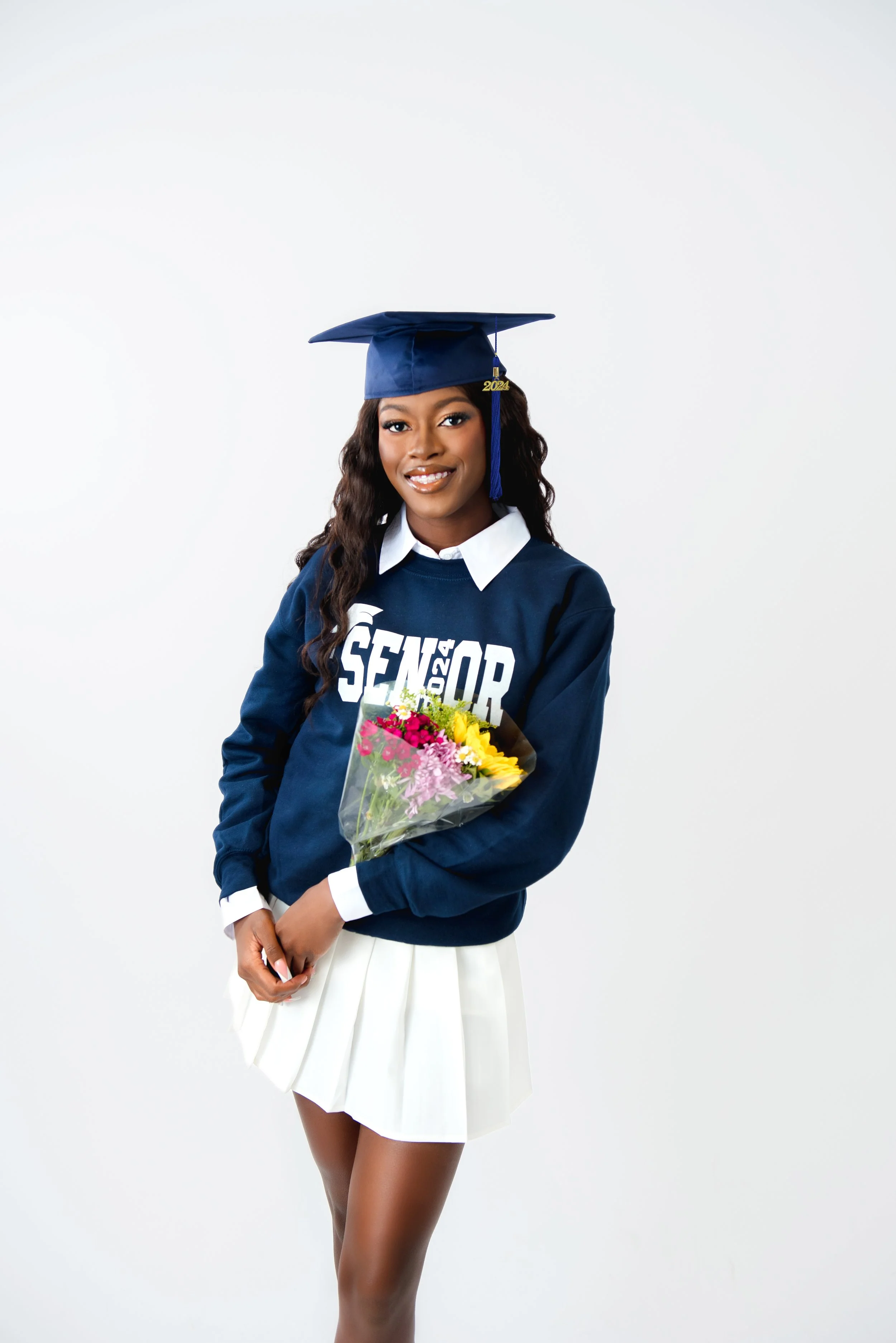 Young woman in graduation cap and gown holding a bouquet of flowers smiling at the camera.
