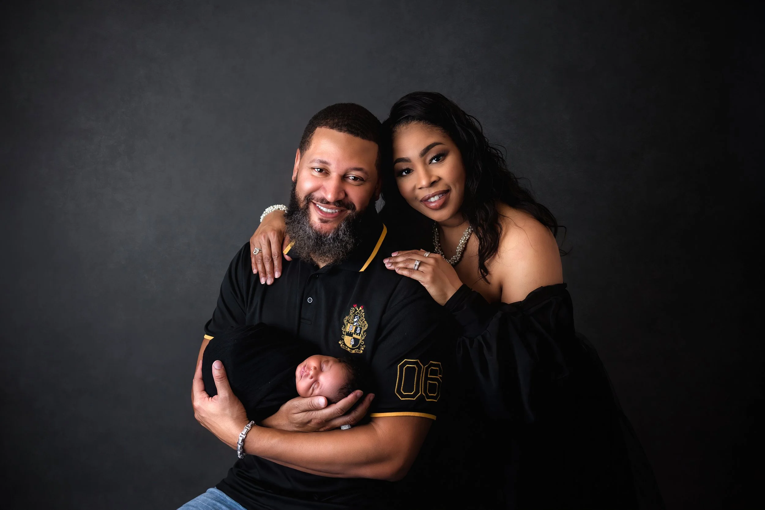 Luxury family newborn portrait of parents with their sleeping baby, photographed against a dramatic dark backdrop in our Spring Branch studio.