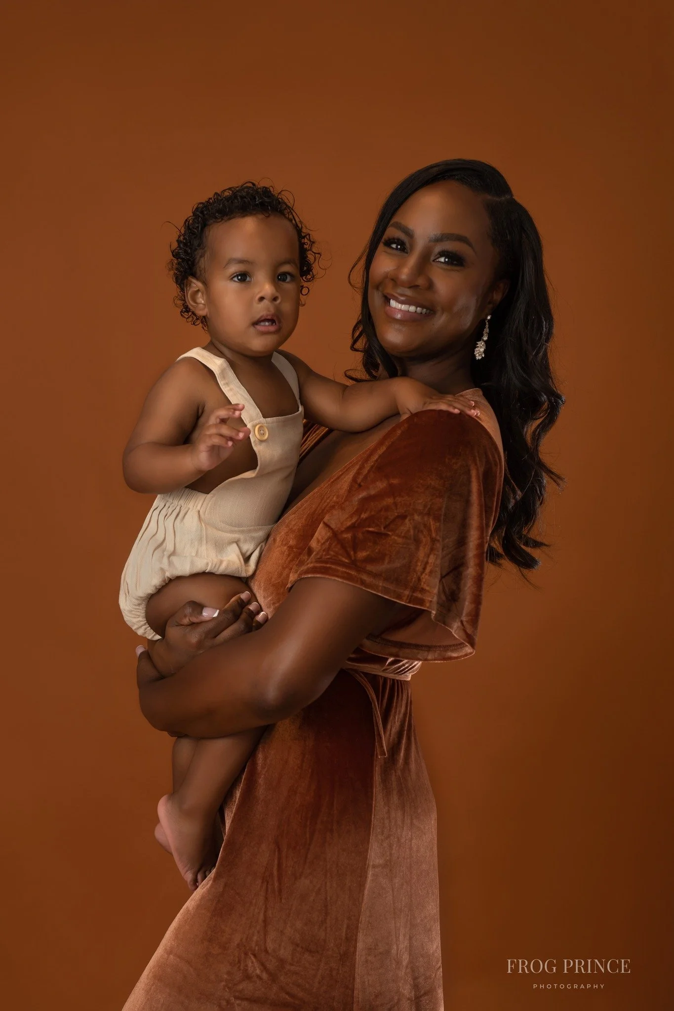A smiling African American woman holding a young girl against a warm brown background.