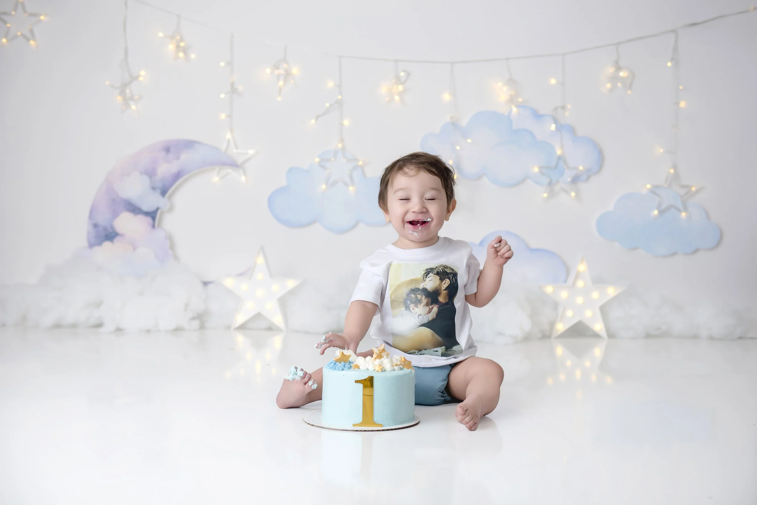 Happy toddler celebrating's first birthday with a cake in a decorated studio with cloud and star decorations in our Spring Branch studio.