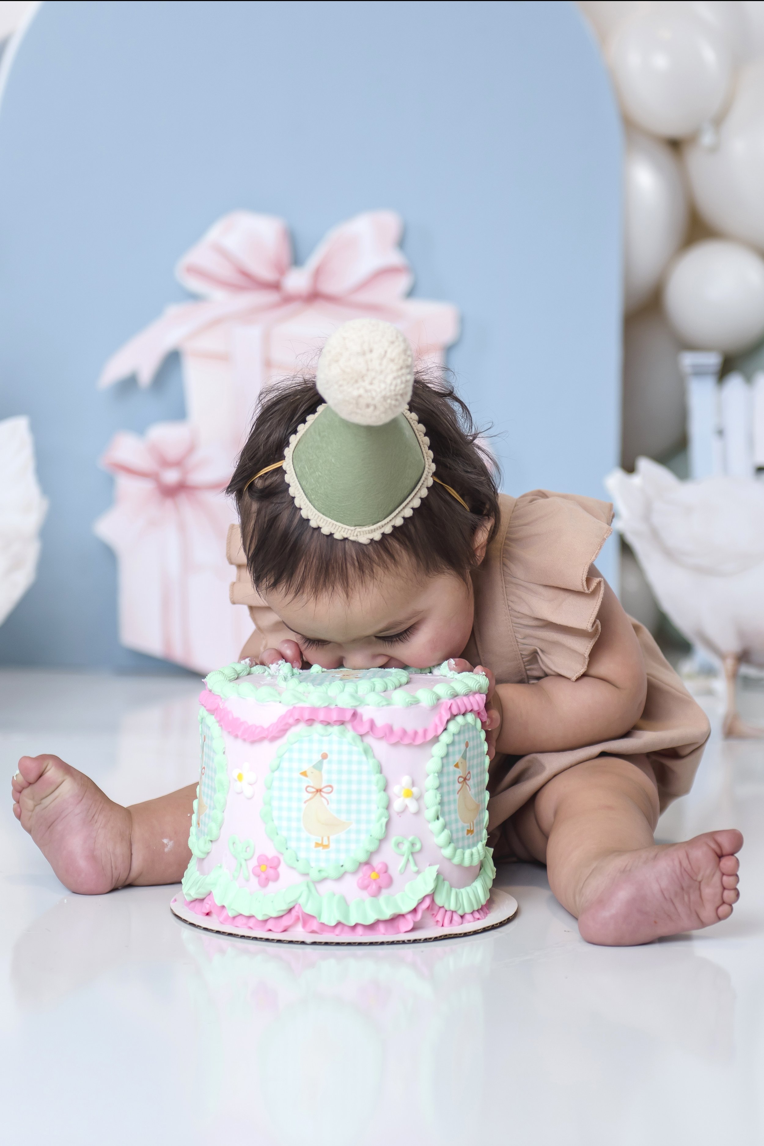 Young girl with a party hat kissing a decorated birthday cake.